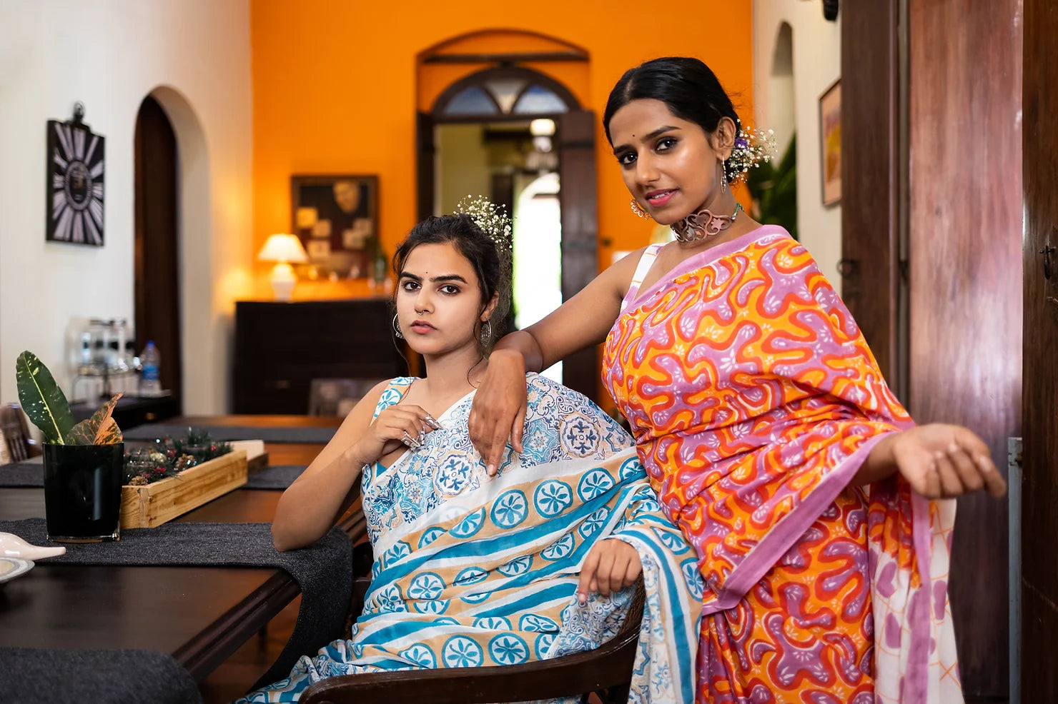 2 women in Mogasu Goa sarees posing at a dining table of an antique Goan house