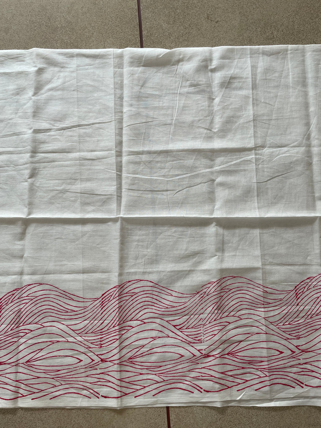White Mogasu saree blouse piece with red wavy pattern on a beige surface.