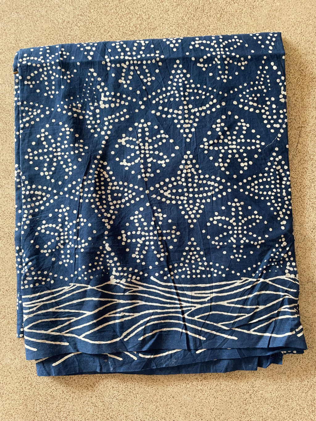 Folded fabric with blue and white pattern on a beige surface. Mogasu’s Starry Surf mul cotton saree blouse piece.