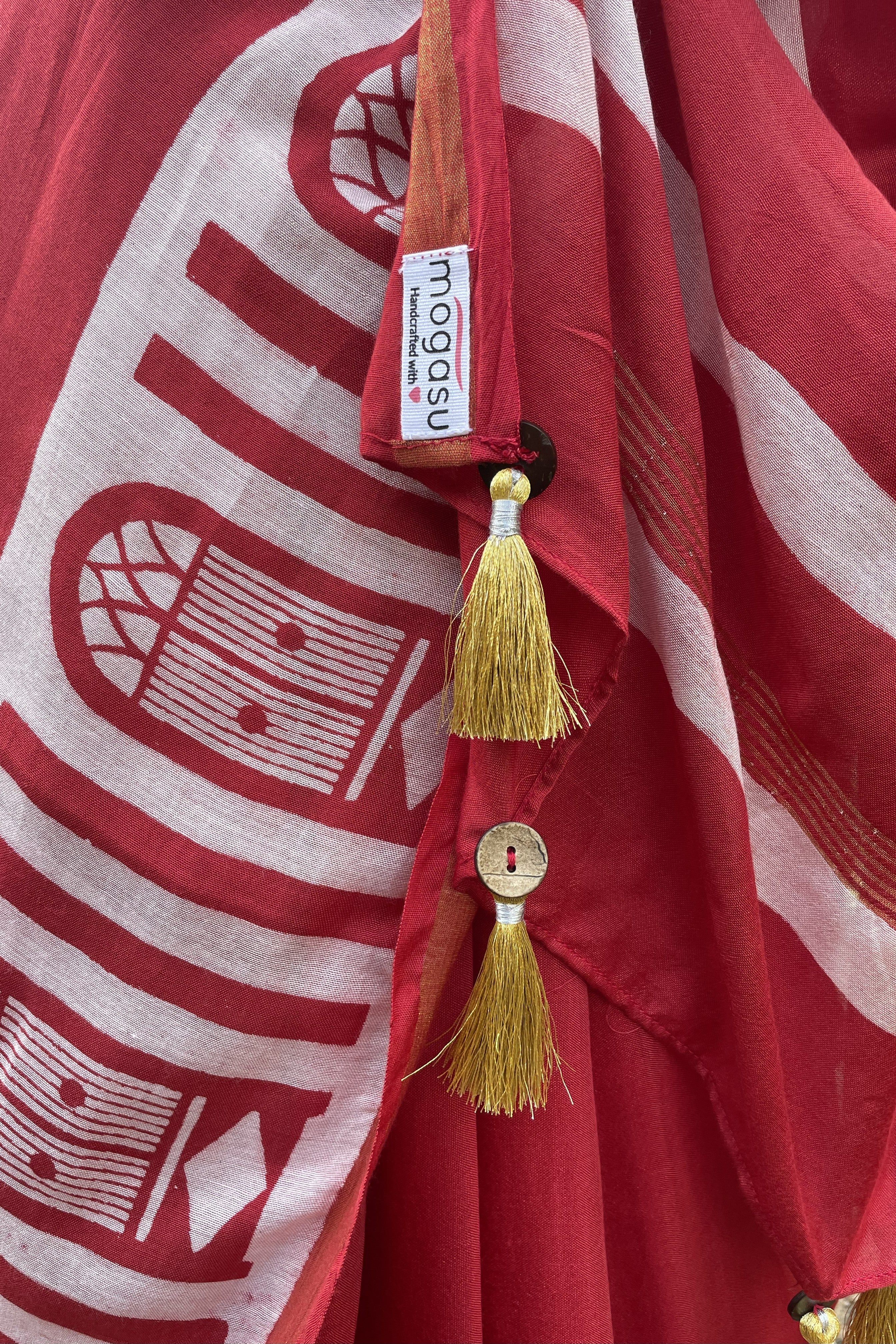Red Mogasu saree with white Goan window patterns and gold tassels, featuring a visible brand label.