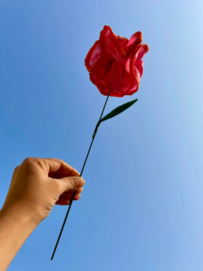 Hand holding a pink fabric rose against a clear blue sky. Mogasu’s initiative to reduce textile waste and convert it into something beautiful