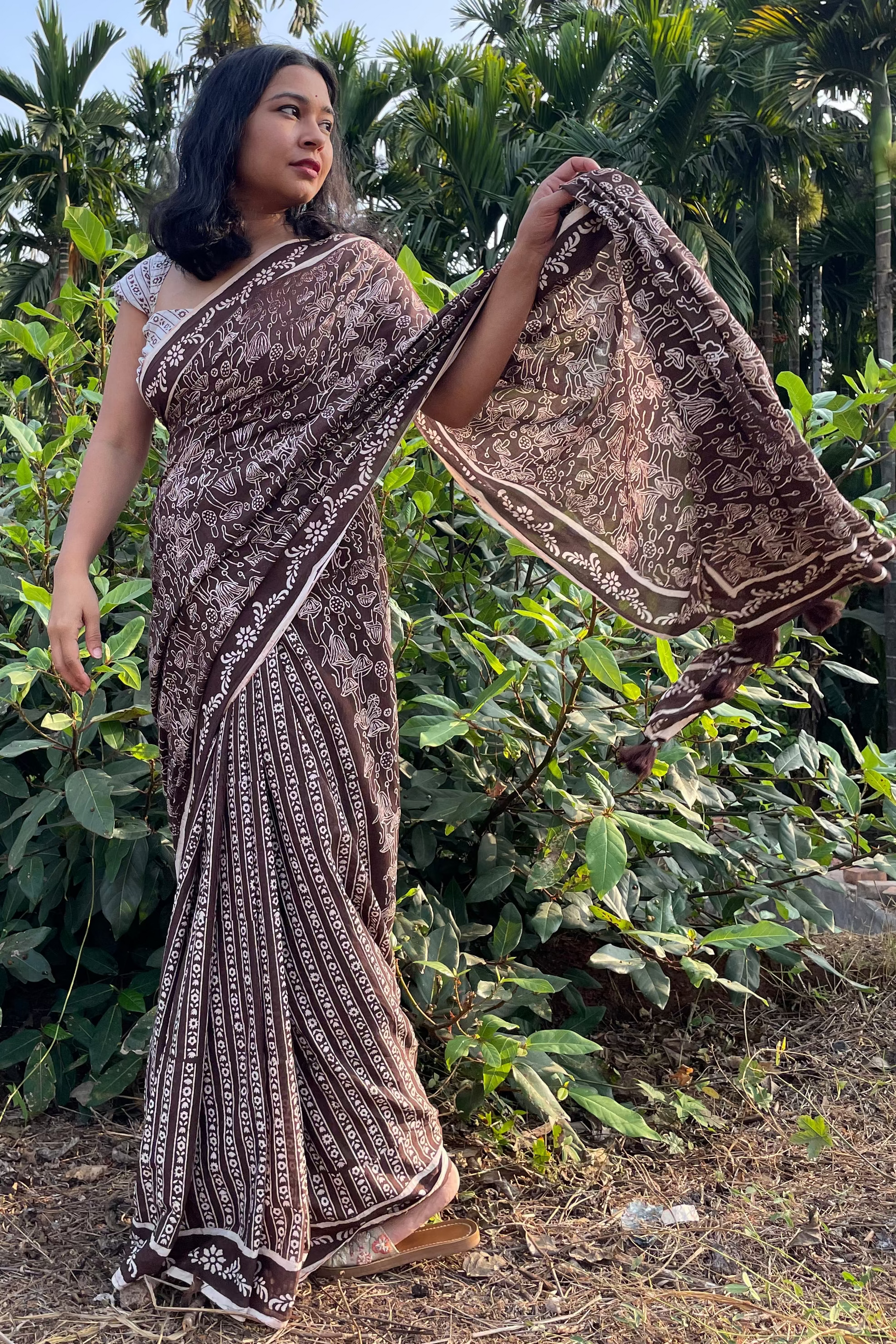 Woman in a mushroom patterned Mogasu mul cotton saree standing outdoors with greenery in Goa.