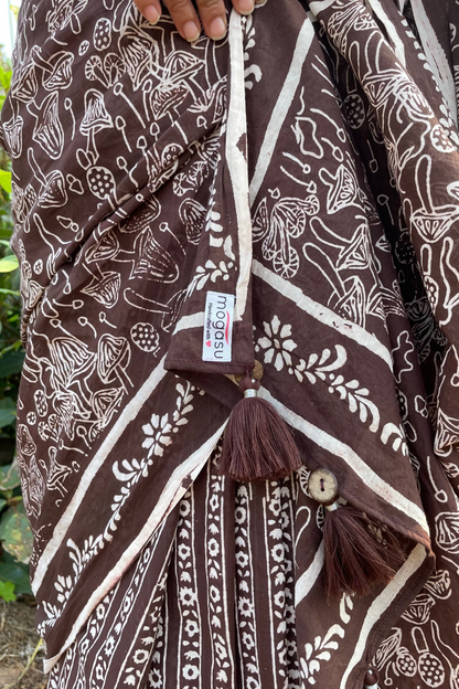 Brown and white mushroom patterned saree with a Mogasu brand label, held by a hand against a natural background in Goa.