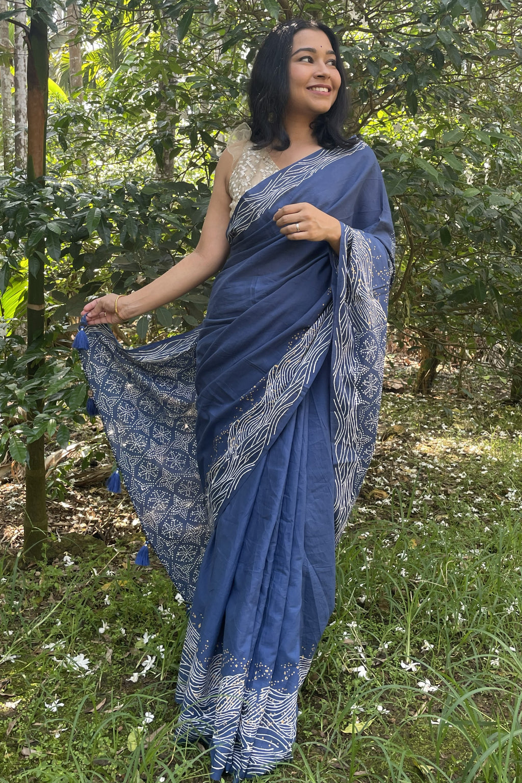 Woman in a blue Mogasu saree with white wave patterns standing in a Goan spice plantation setting