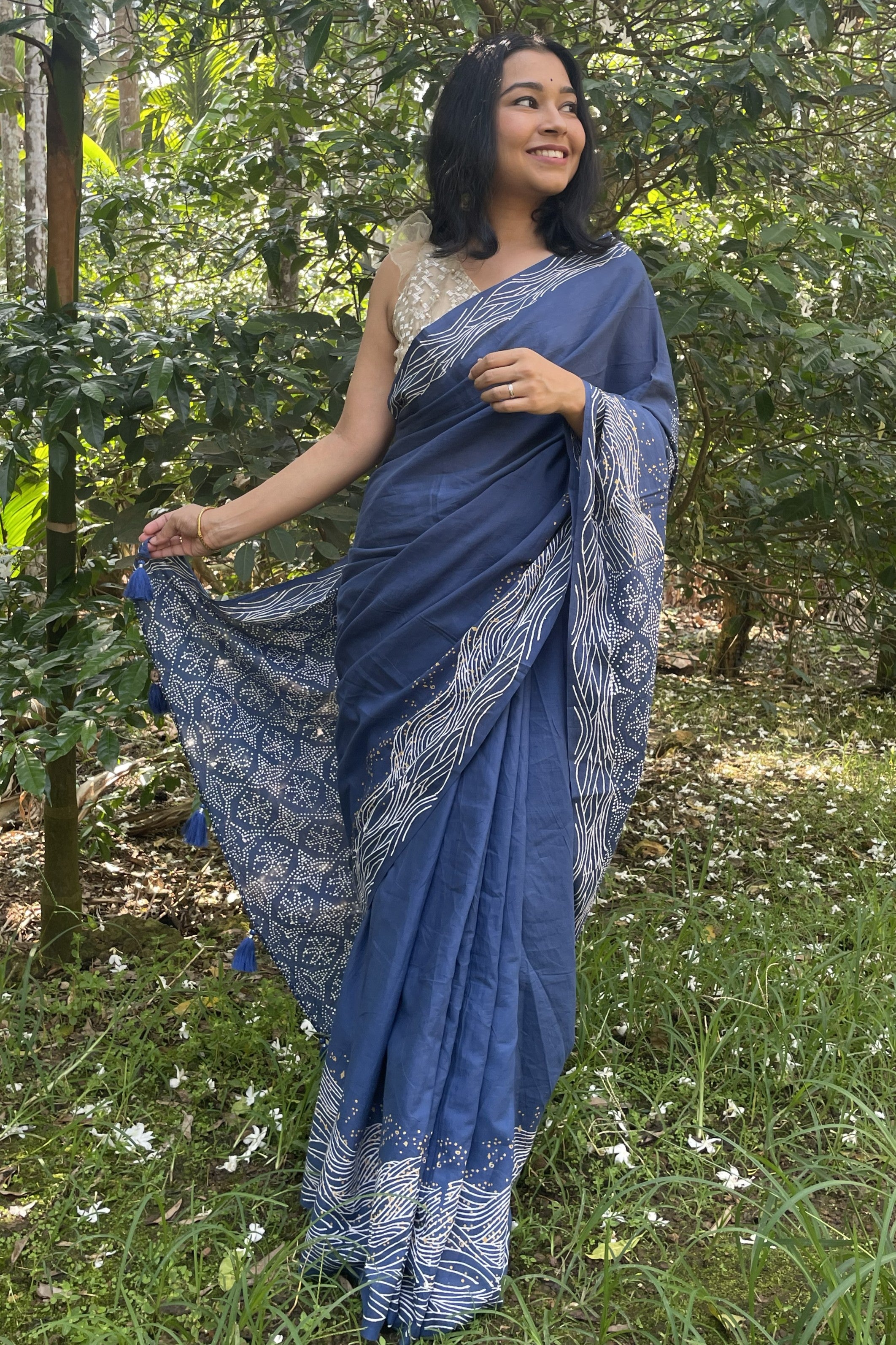 Woman in a blue Mogasu saree with white wave patterns standing in a Goan spice plantation setting