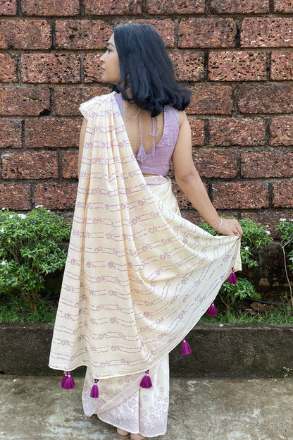 Woman wearing a Mogasu cream saree with purple accents in front of a brick wall in Goa.