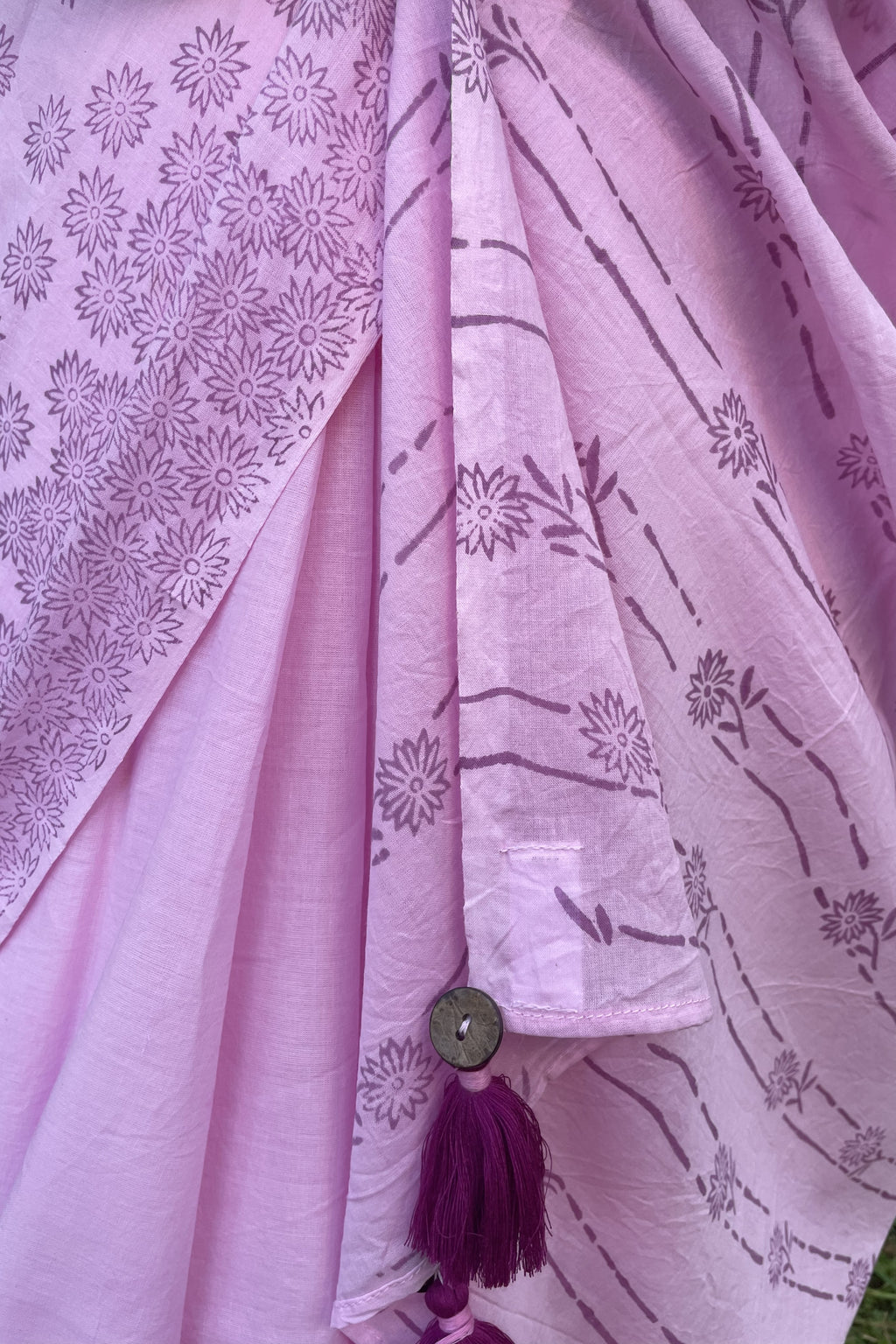 Close-up of a Mogasu pink saree with floral patterns and a button with tassels at pallu.