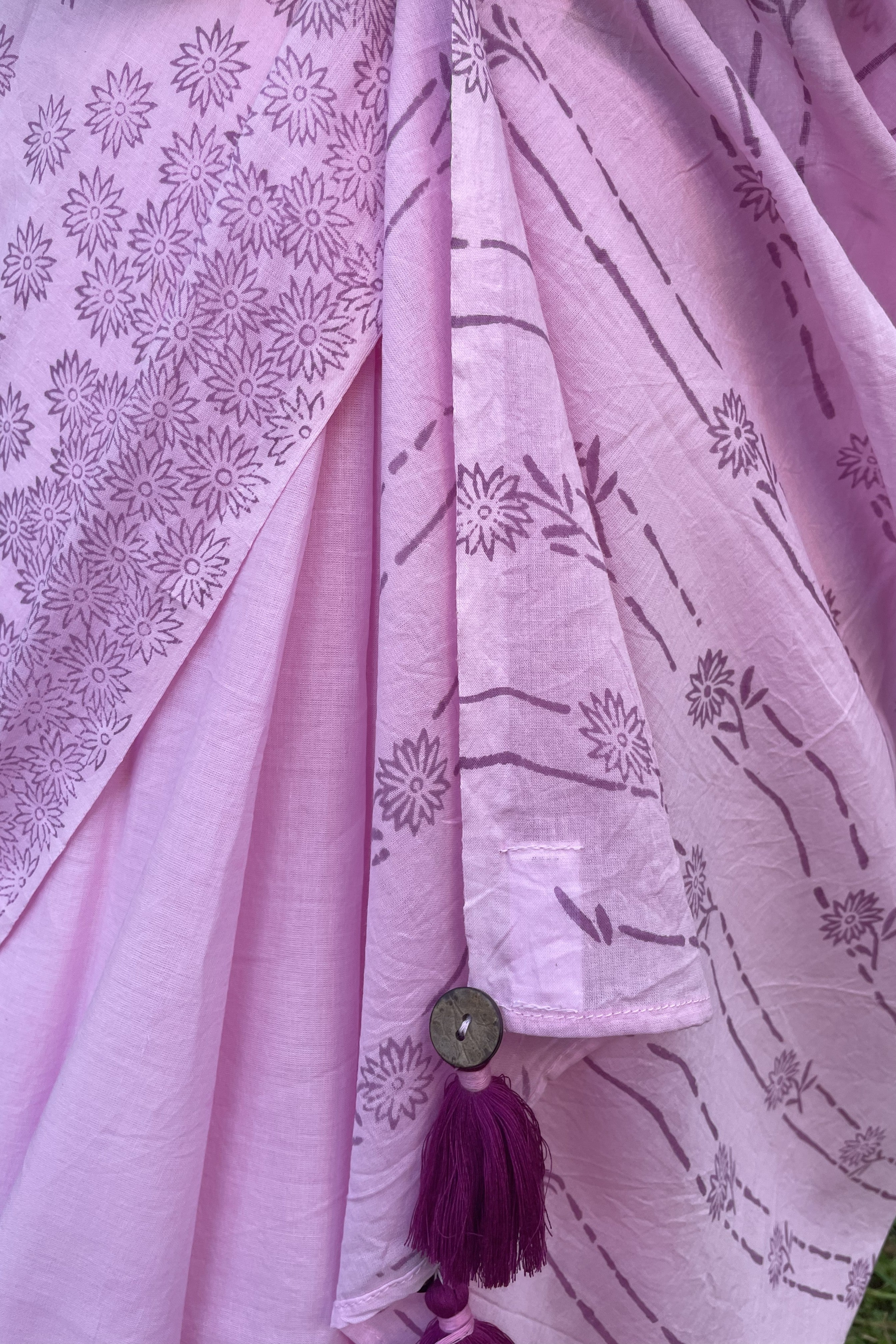 Close-up of a Mogasu pink saree with floral patterns and a button with tassels at pallu.