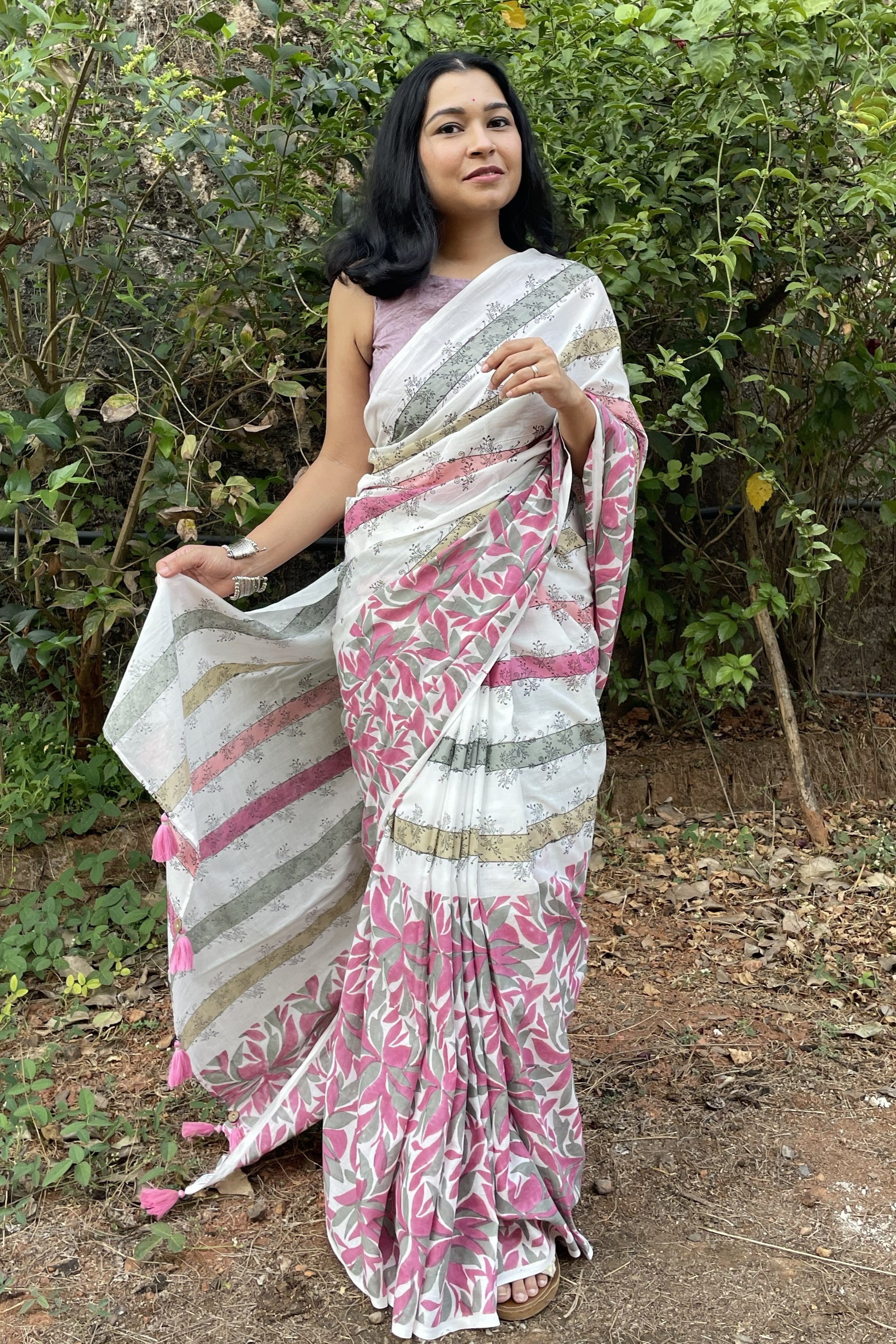 Woman wearing a Mogasu white and pink saree with a floral pattern, standing outdoors in Goa.