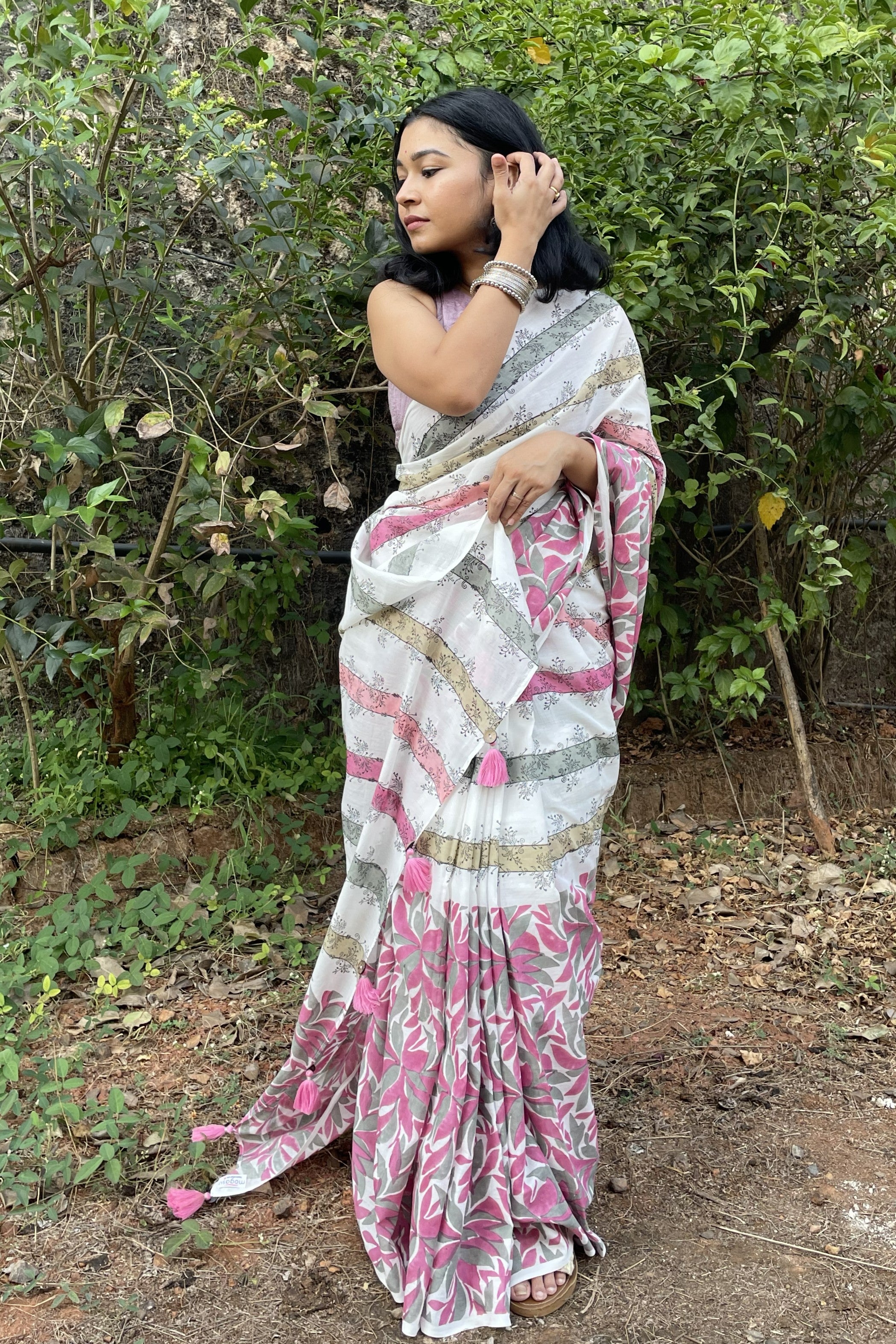 Woman wearing a Mogasu white and pink mul cotton saree with patterns in a natural setting in Goa