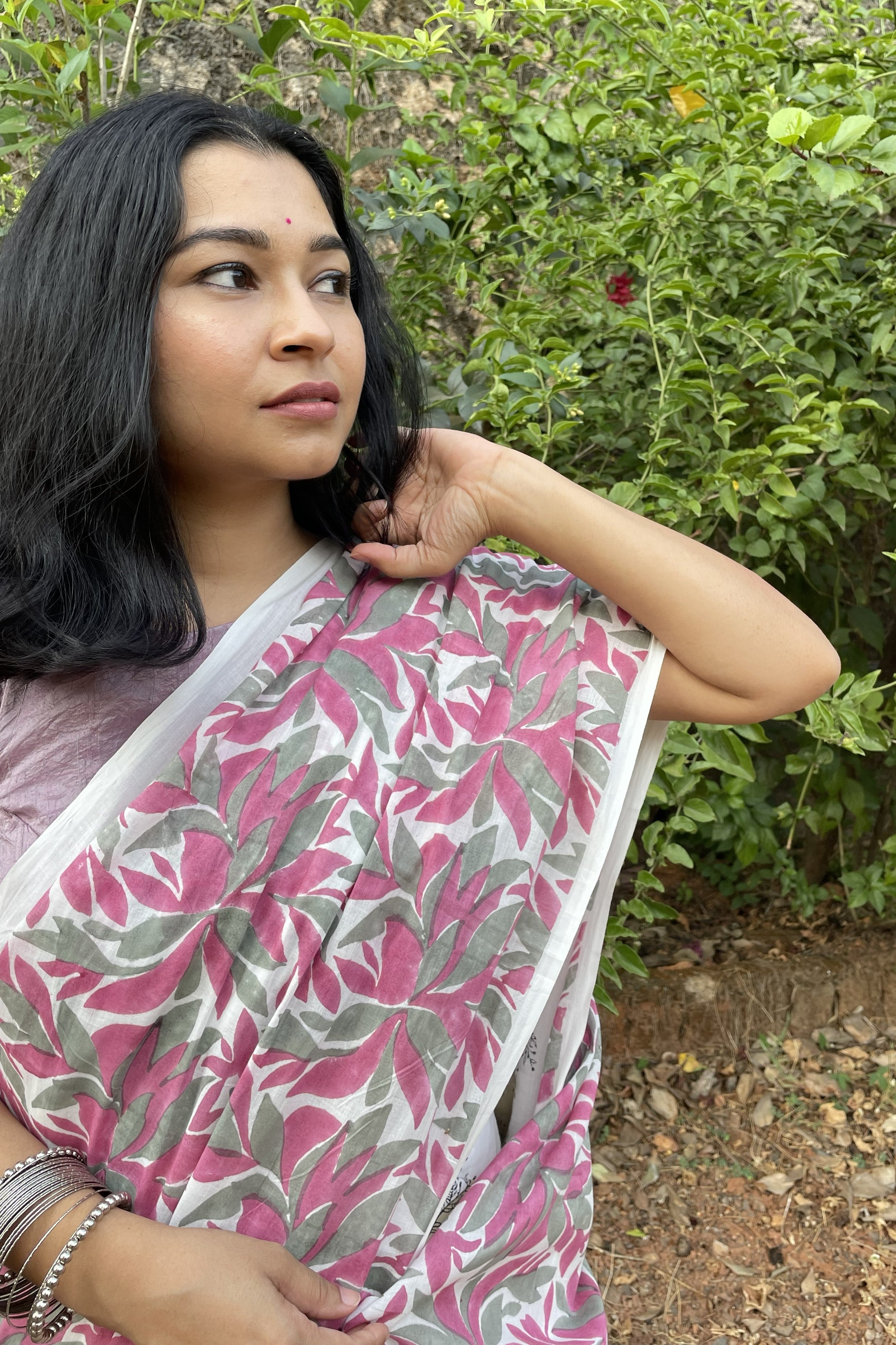 Woman wearing a Mogasu pink and gray floral saree outdoors with greenery in the background in Goa