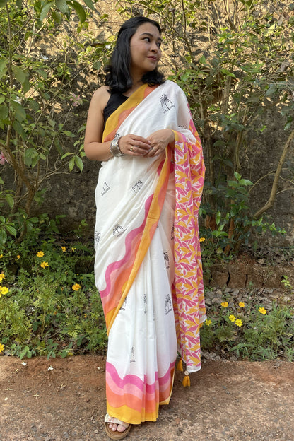 Woman wearing a white Mogasu mul cotton saree with pink and yellow patterns, standing outdoors in Goa.