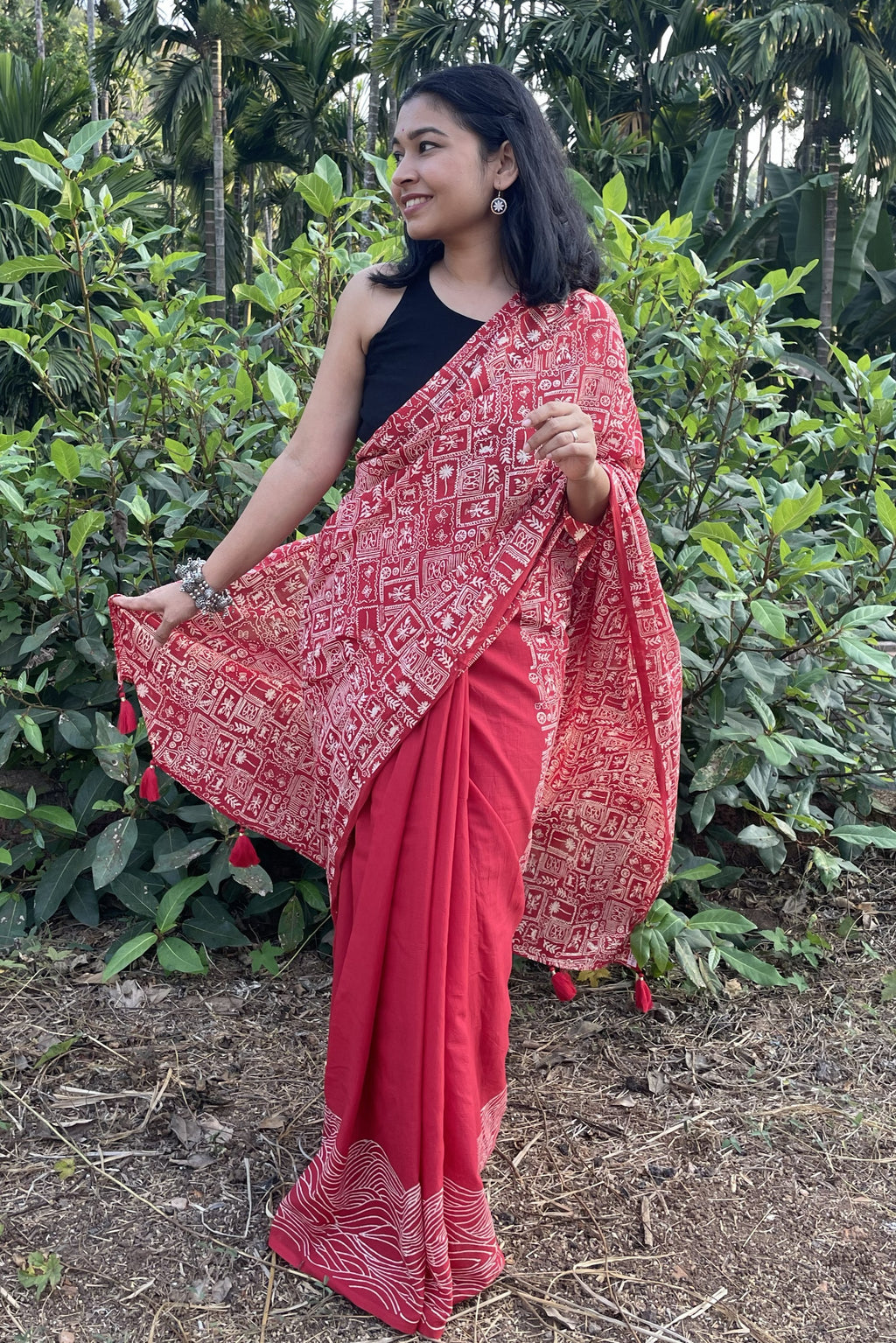 Woman wearing a red mul cotton Mogasu saree with a patterned border in a natural setting in Goa