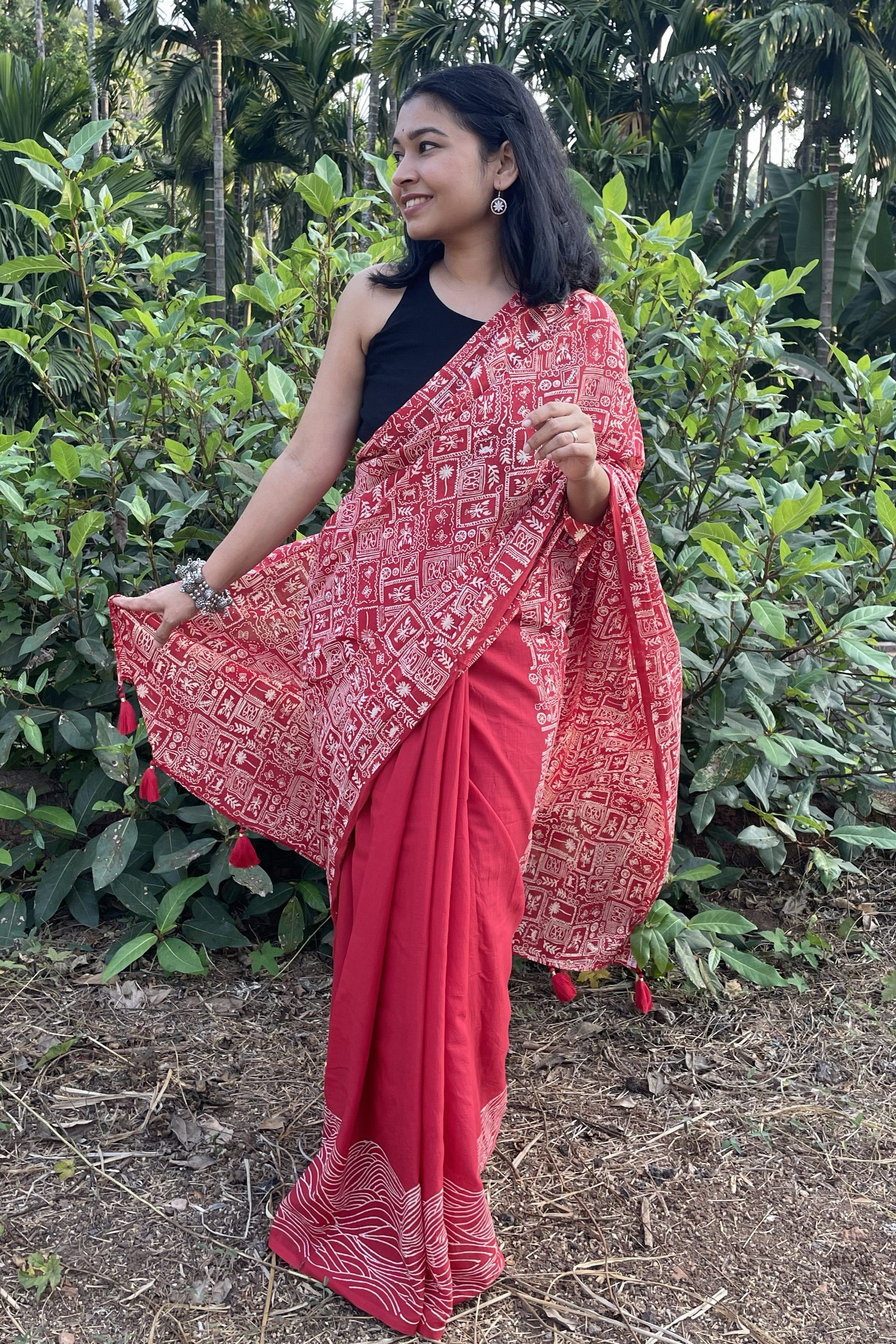 Woman wearing a red mul cotton Mogasu saree with a patterned border in a natural setting in Goa
