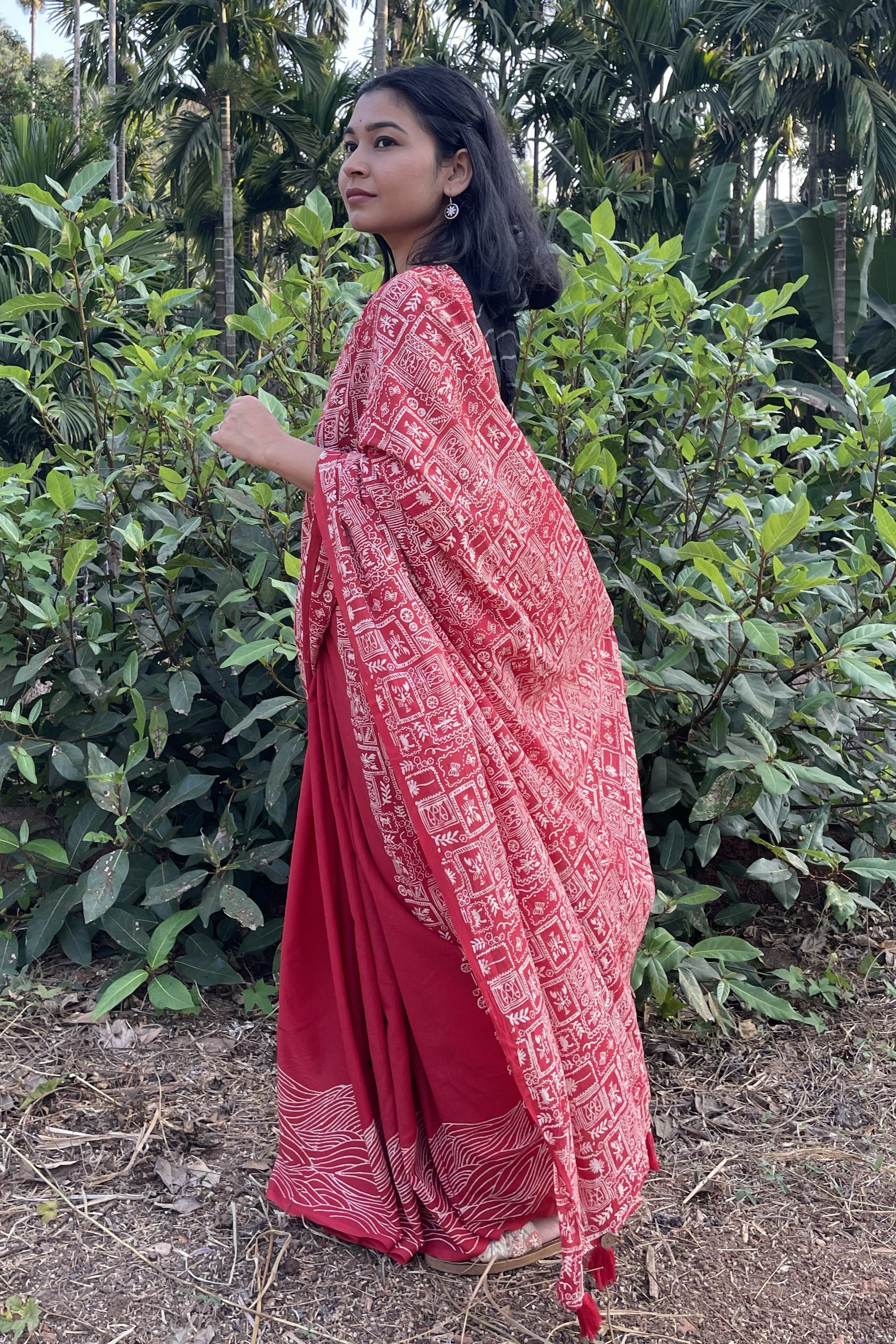 Woman wearing a red Mogasu saree with white patterns standing in a natural setting in Goa.