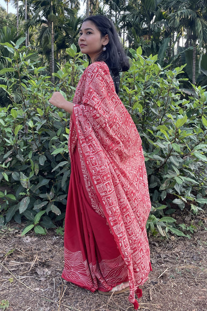 Woman wearing a red Mogasu saree with white patterns standing in a natural setting in Goa.