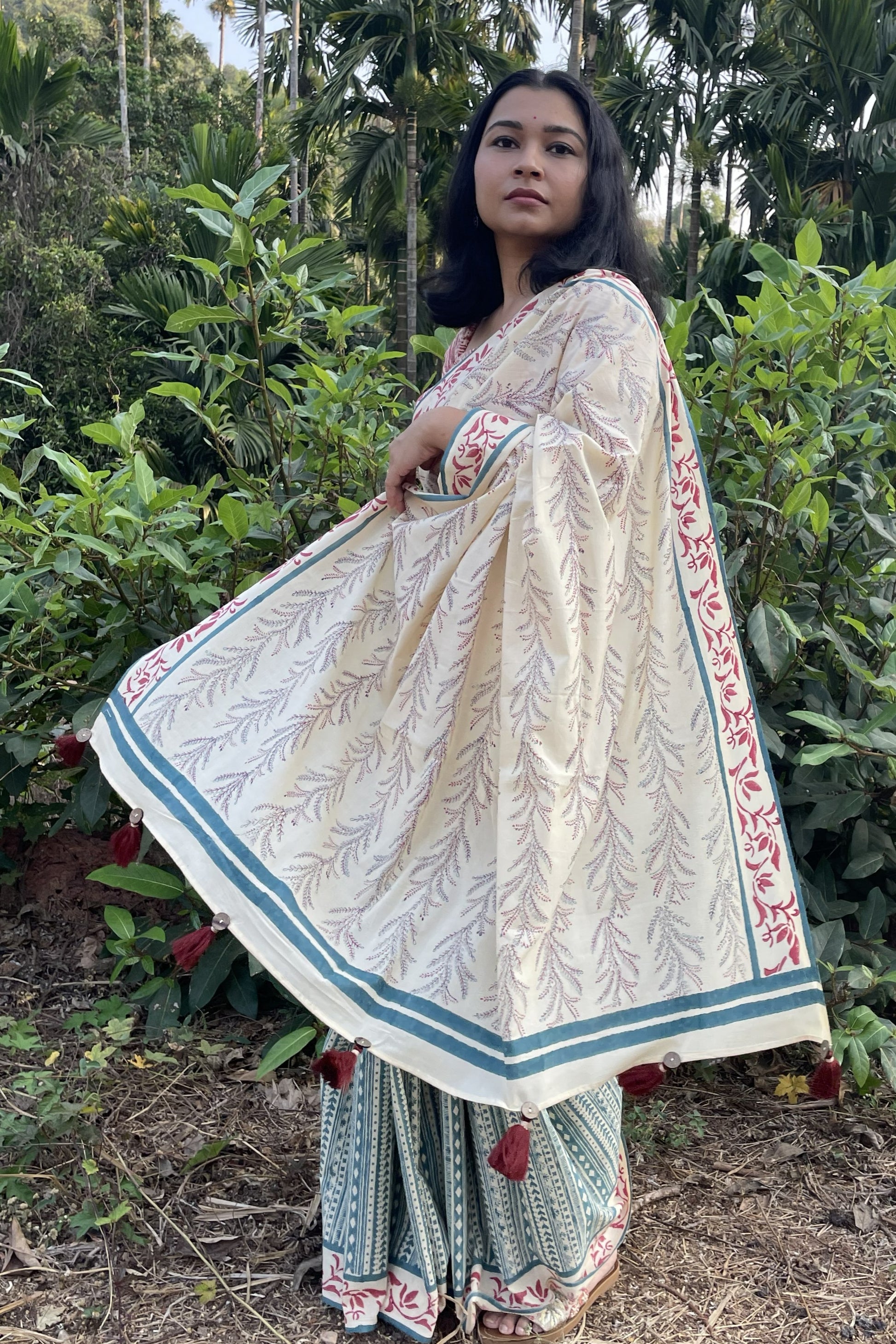 Woman in a Mogasu mul cotton saree standing in a natural setting with greenery.