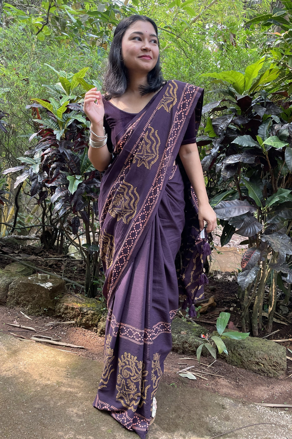 Woman in a Mogasu’s Noa purple mul cotton saree with gold patterns standing in a forest setting