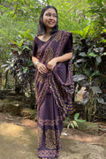 Woman in a traditional purple and gold saree standing in a forest setting in Goa. She as draped Mogasu’s mul cotton saree.
