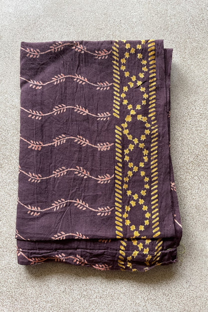 Folded purple blouse piece with yellow patterns on a gray surface. Mogasu’s blouse piece for Noa saree in mul cotton.