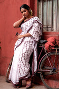 Woman in a light pink Mogasu saree with red patterns leaning against a bicycle next to a red wall.