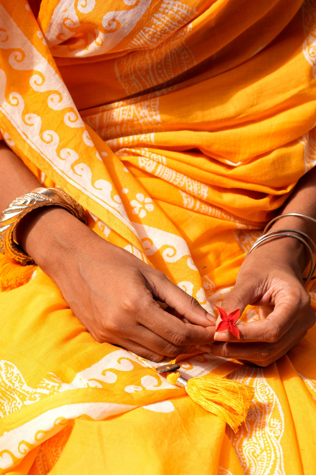 Person wearing a bright yellow Mogasu Brosa mul cotton saree with white patterns, holding a small red object.