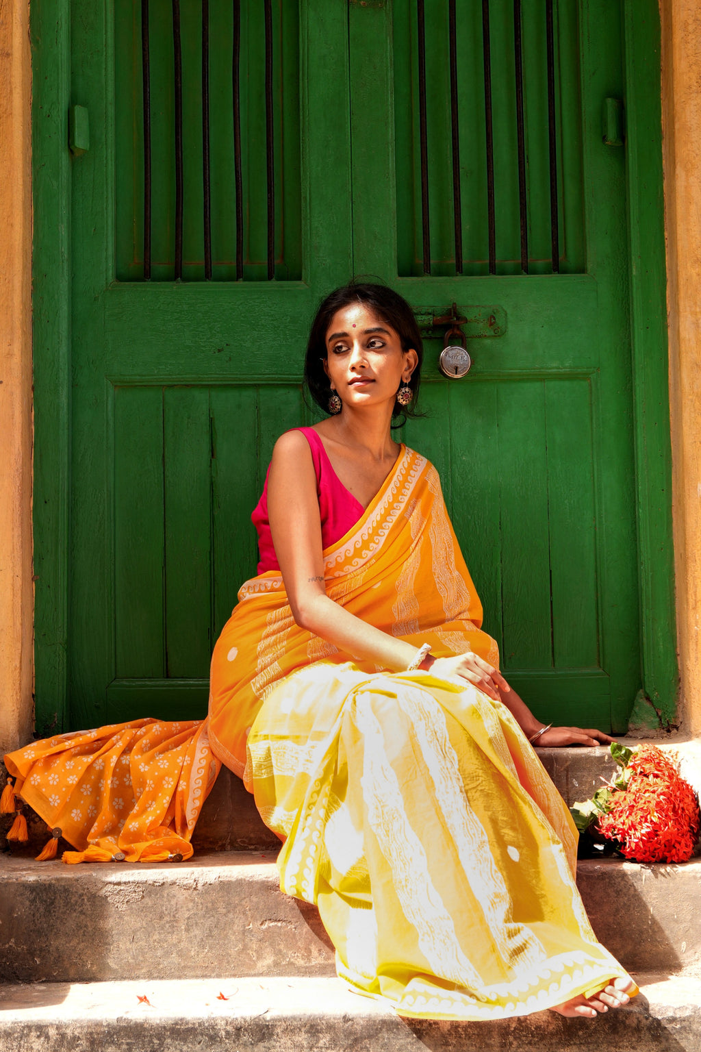 Woman in a yellow Mogasu Brisa mul cotton saree sitting on steps with a green door in the background