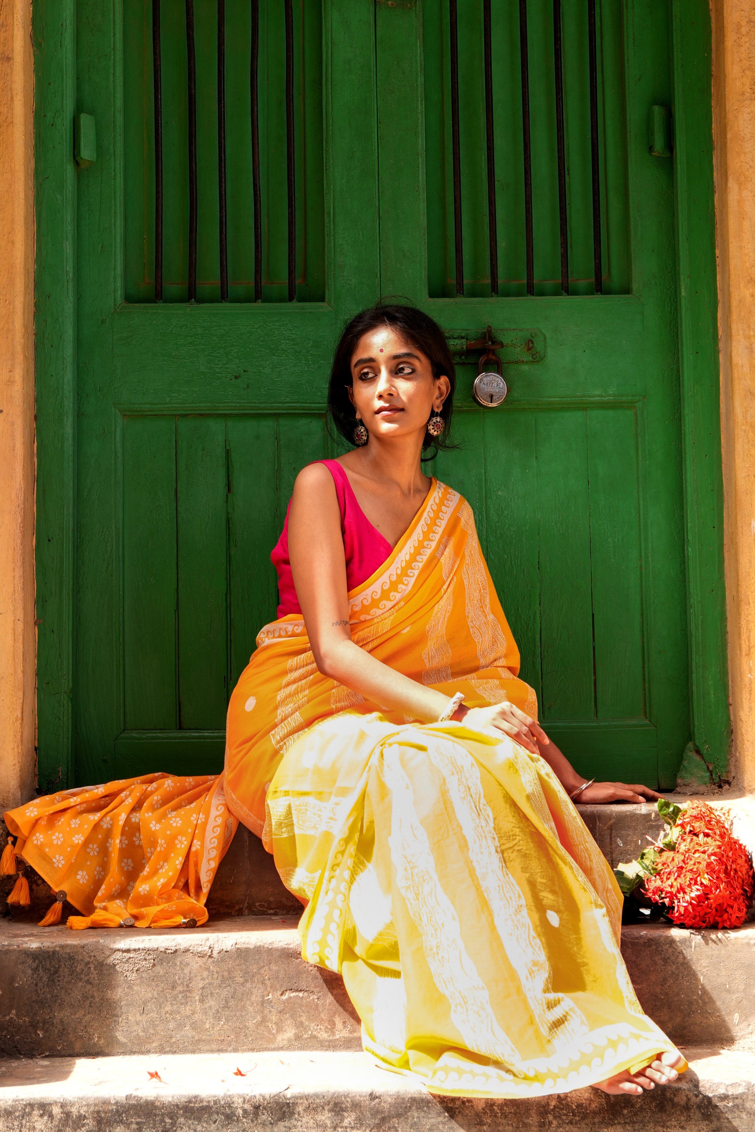 Woman in a yellow Mogasu Brisa mul cotton saree sitting on steps with a green door in the background