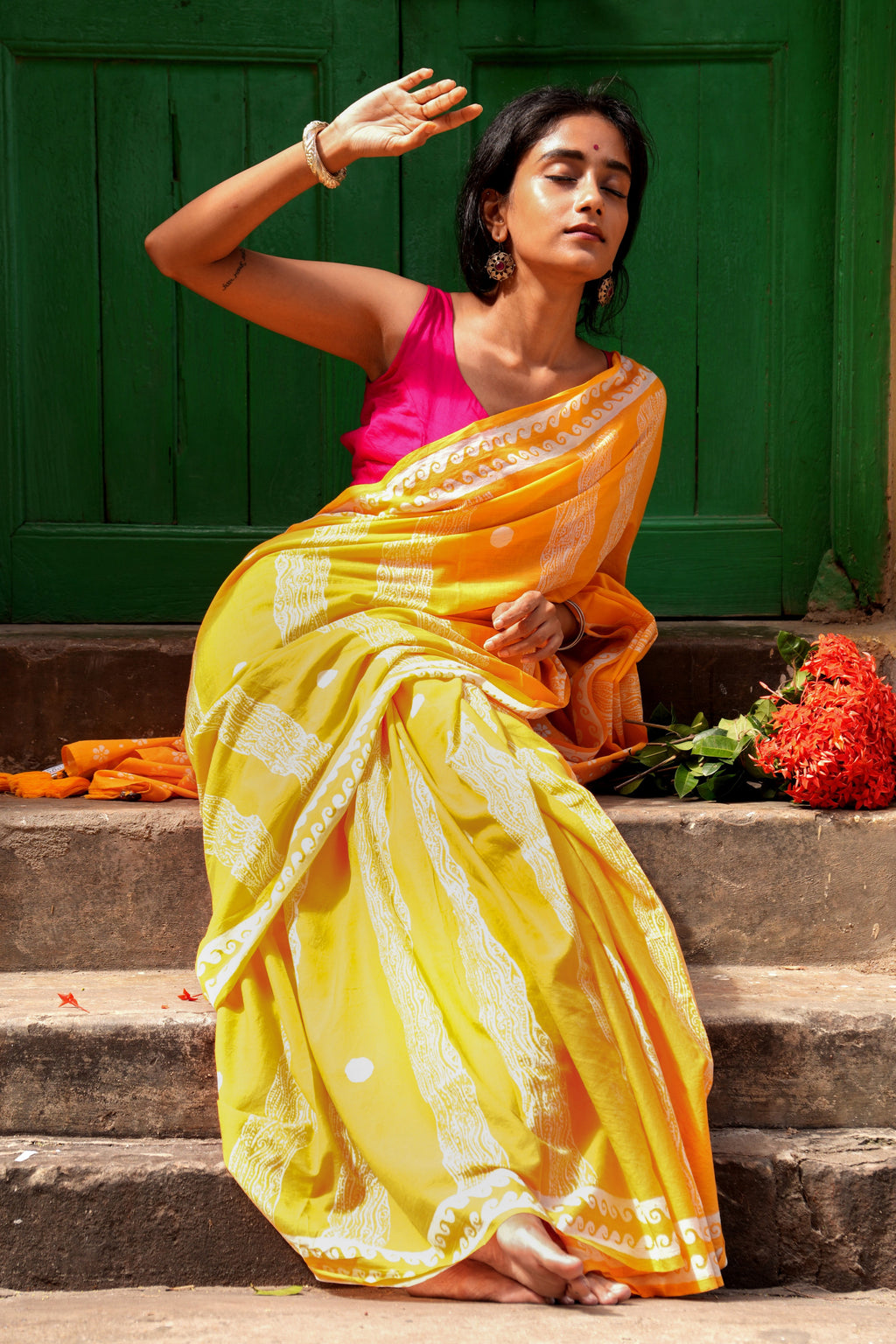Woman in a yellow Mogasu Brisa saree sitting on steps with a green door in the background