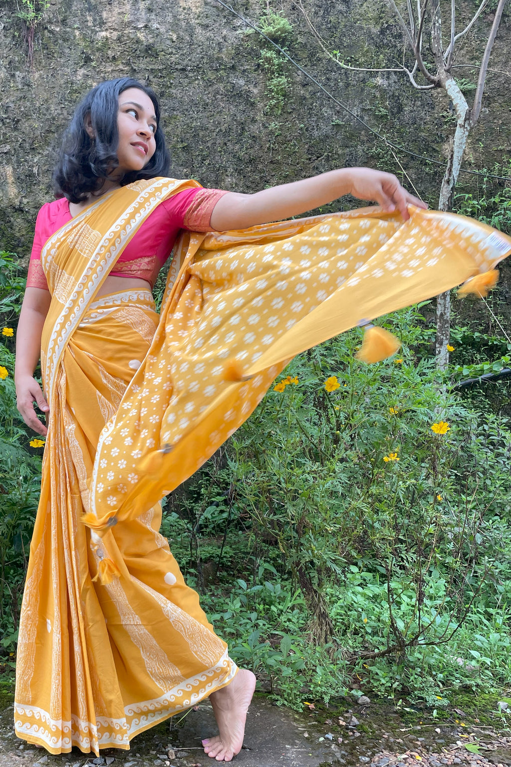 Woman in a yellow Mogasu saree with white patterns standing outdoors against a natural background in Goa