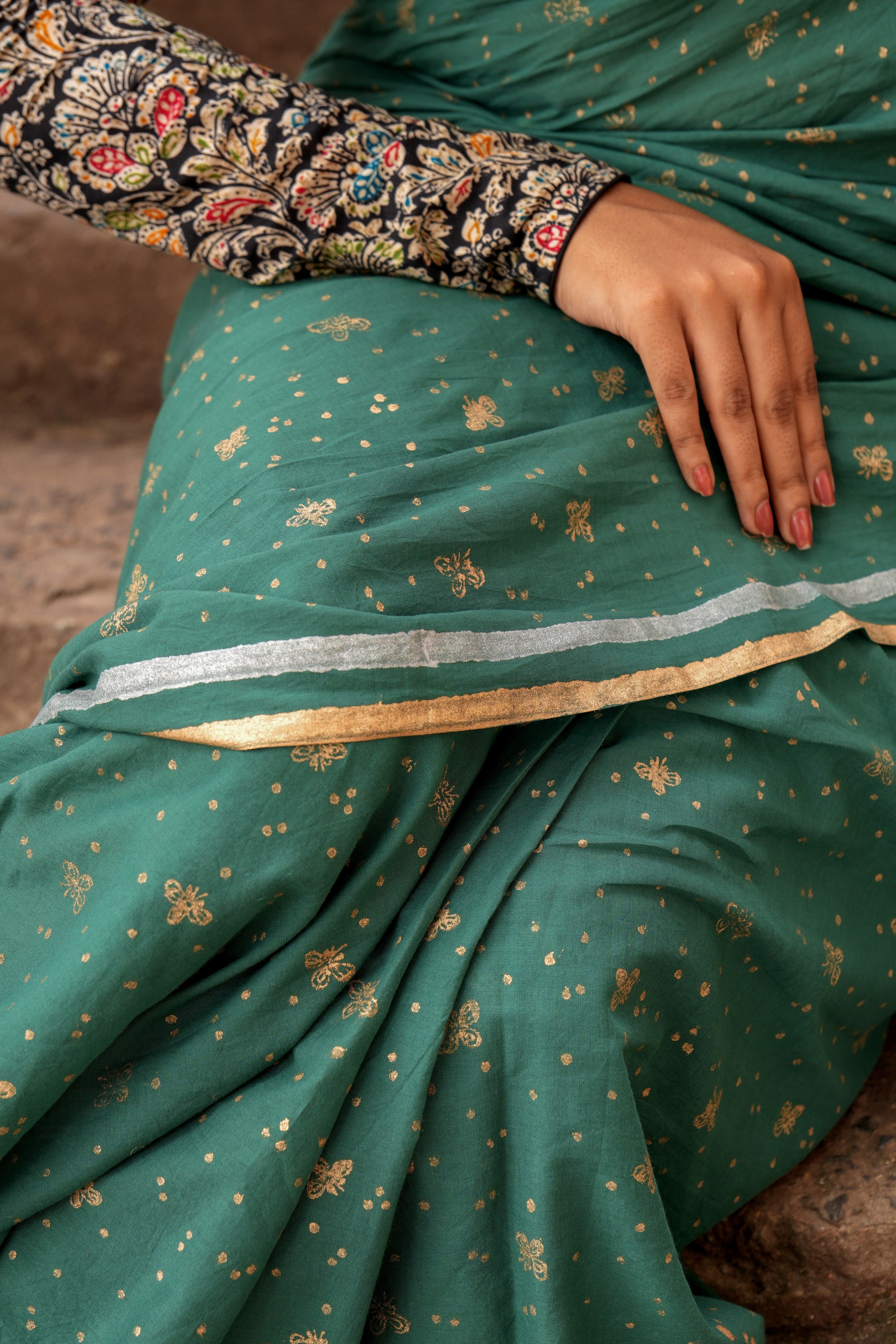Green Mogasu saree with gold fire fly patterns draped over a person, sitting on a brown surface.