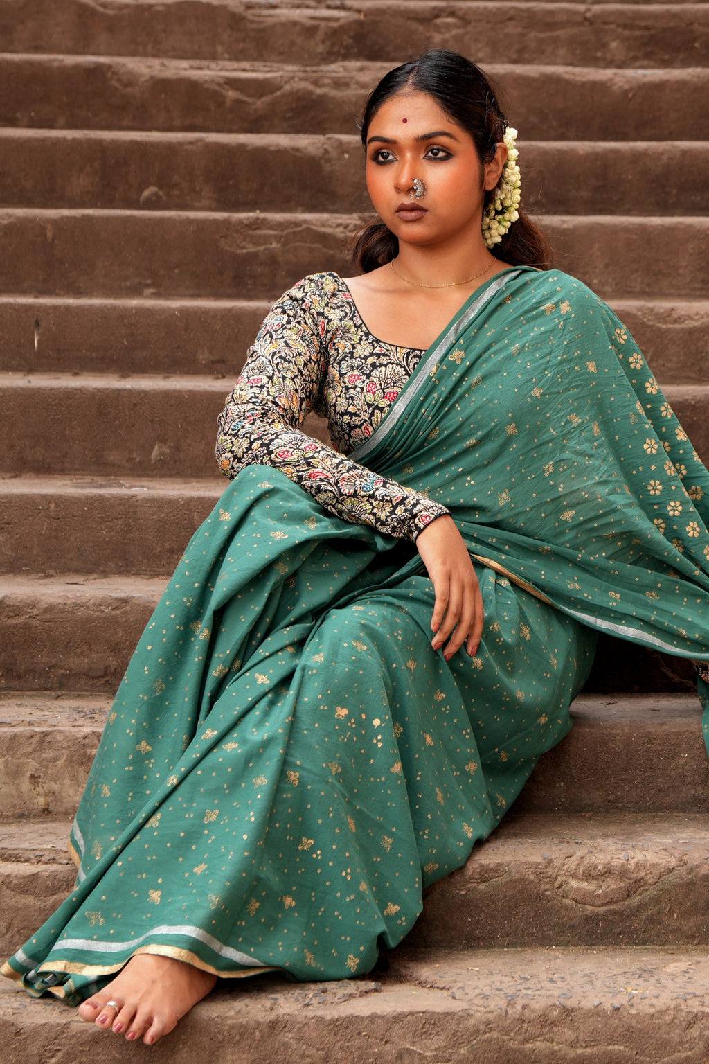 Woman in a green Mogasu Cazulo saree sitting on stone steps