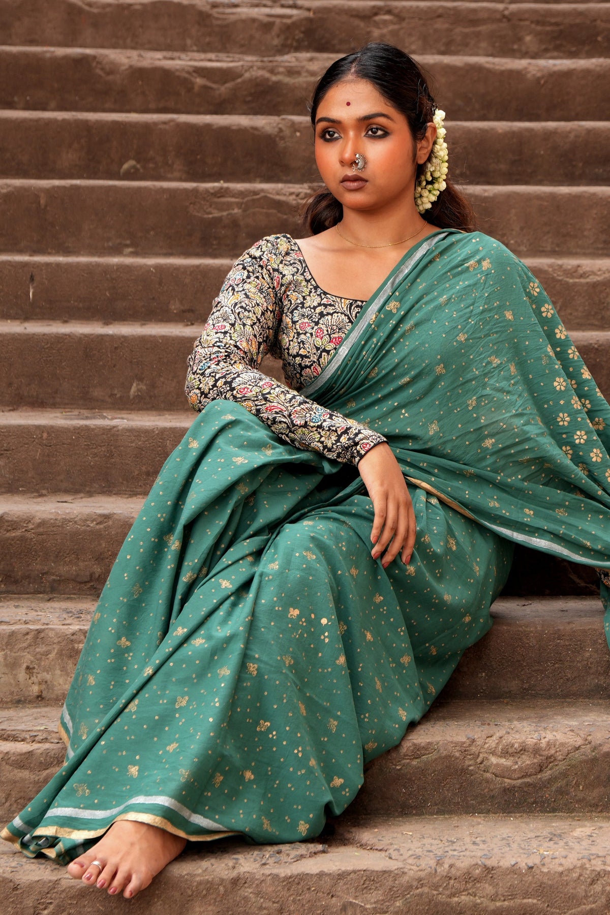 Woman in a green Mogasu Cazulo saree sitting on stone steps