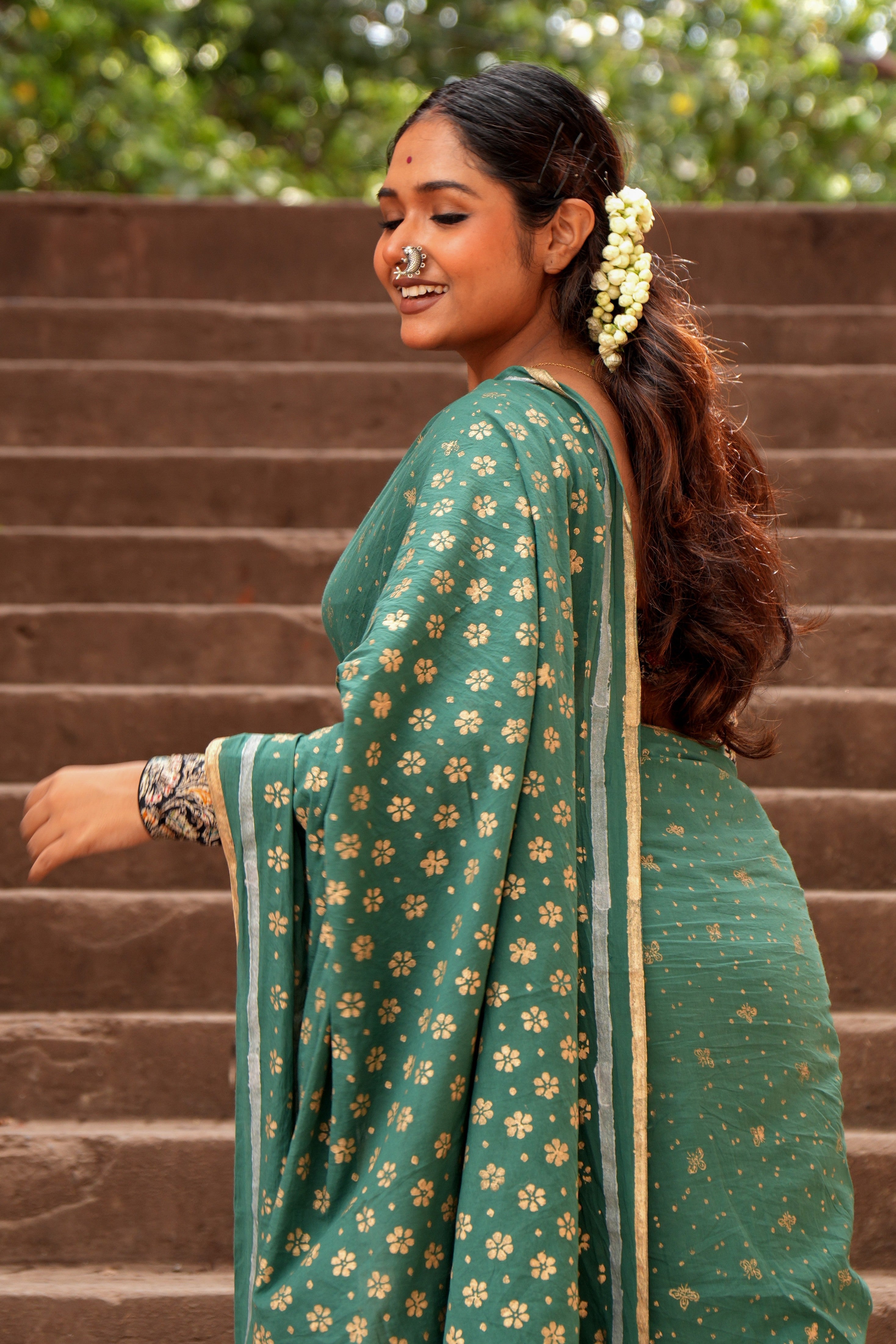 Woman in a green Mogasu Cazulo saree with floral patterns standing on steps outdoors
