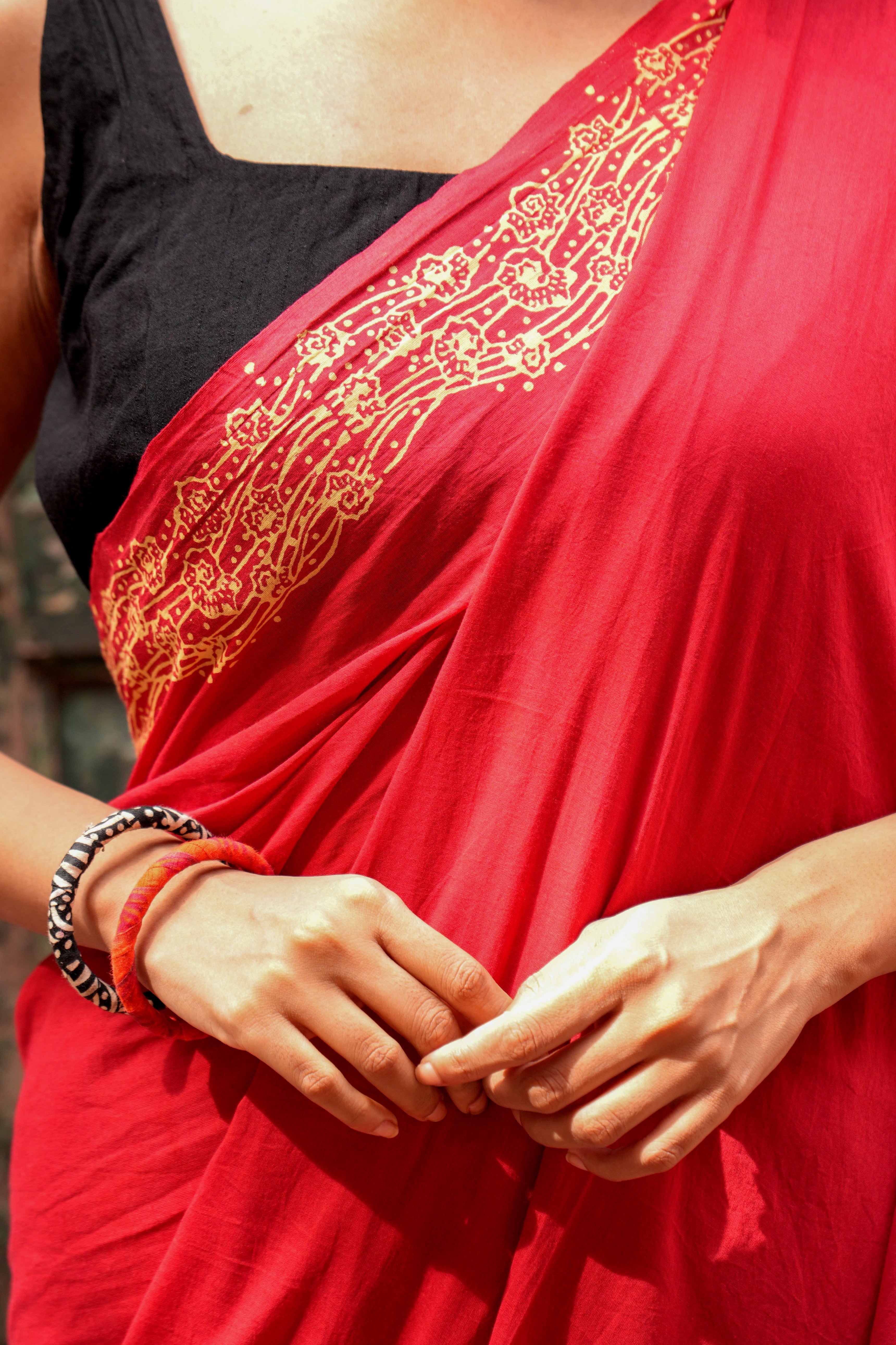 Red Mogasu Lhaar saree with gold pattern 
worn by a person, close-up of hands and saree.