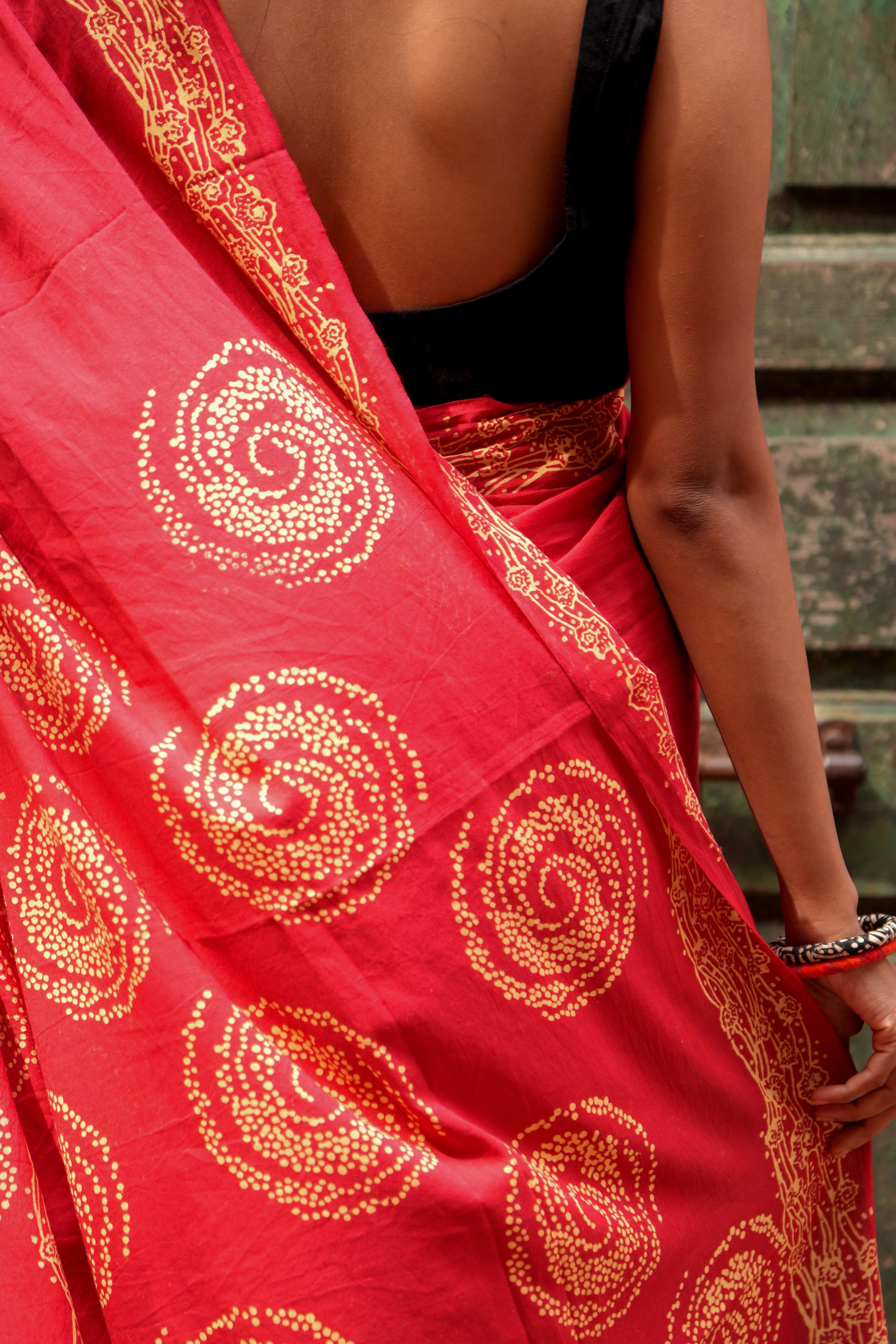 Red Mogasu Lhaar saree with gold patterns worn by a person, with a blurred background