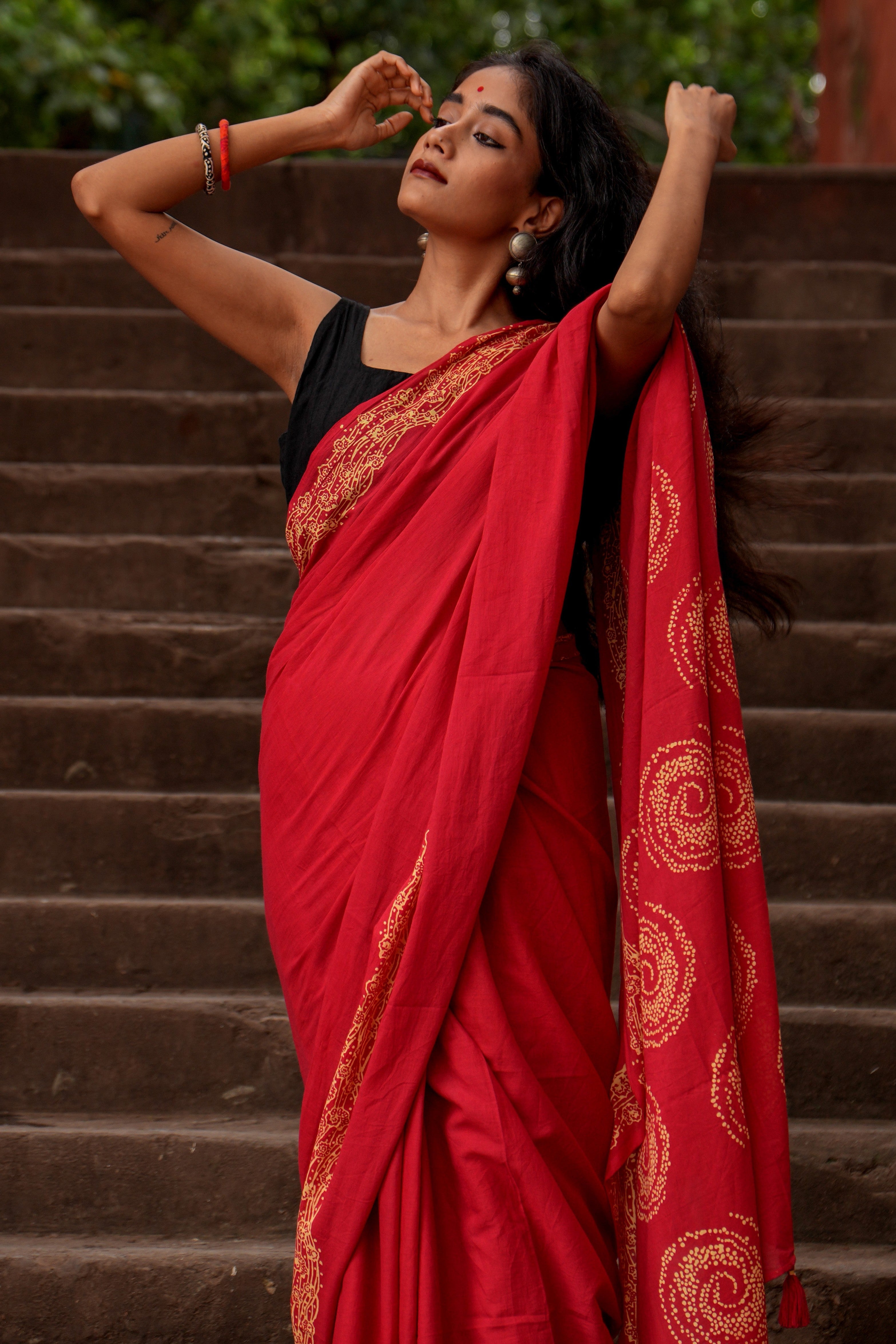 Woman in a red Mogasu Lhaar saree with gold patterns standing on steps outdoors