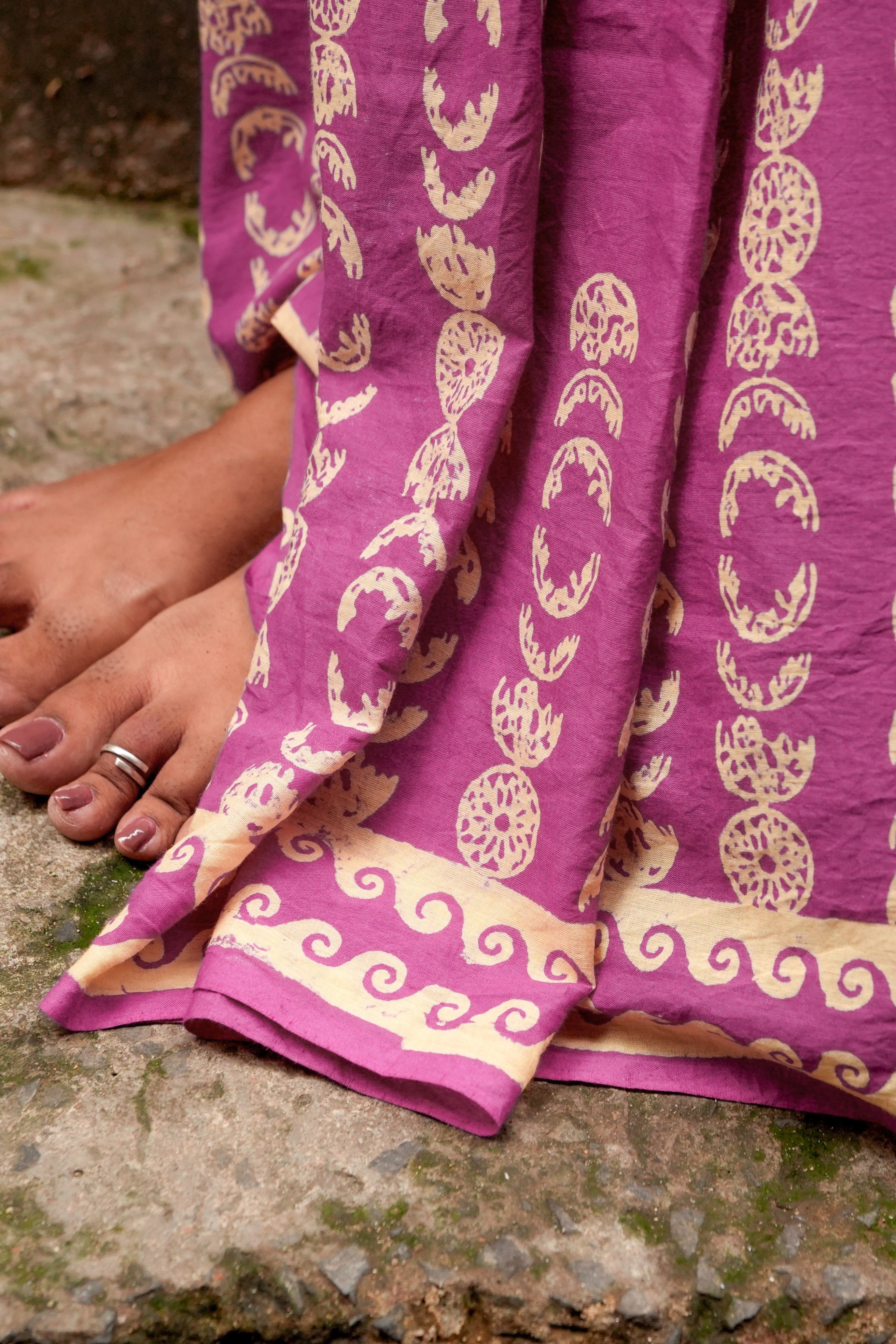 Purple Mogasu saree with gold patterns draped over a person's leg on a stone surface