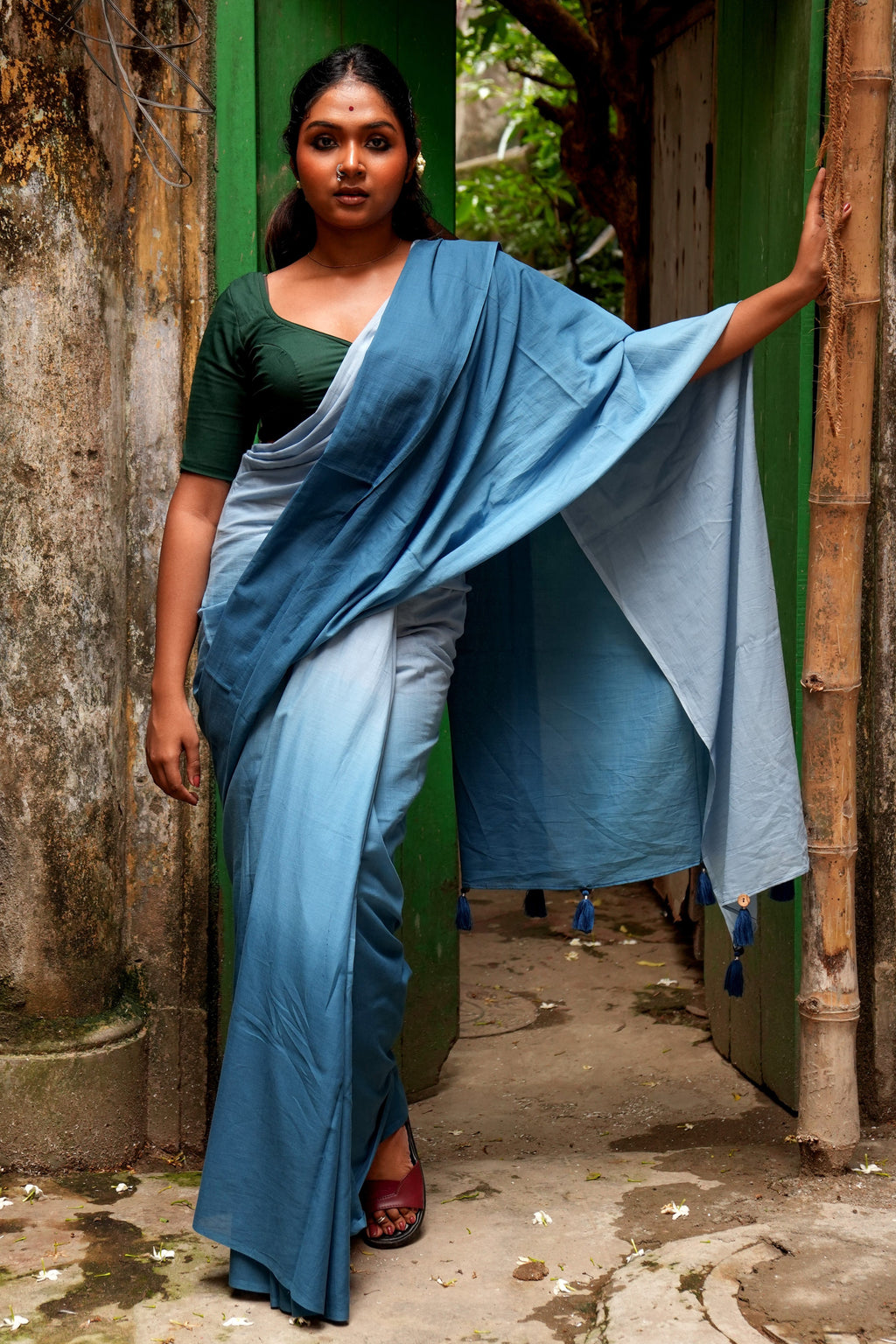 Woman in a blue Mogasu Rati saree standing in a narrow alleyway.