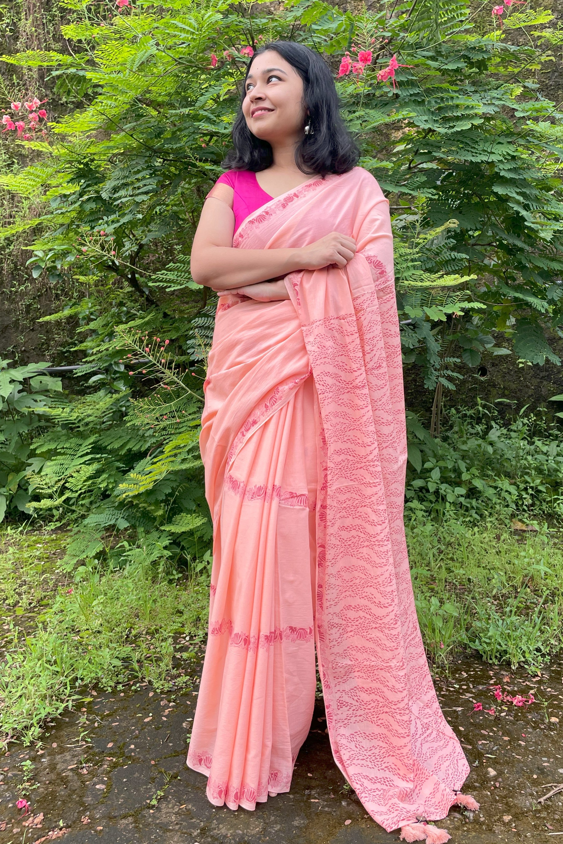 Woman in a peach Mogasu mul cotton saree standing outdoors with greenery in the background in Goa.