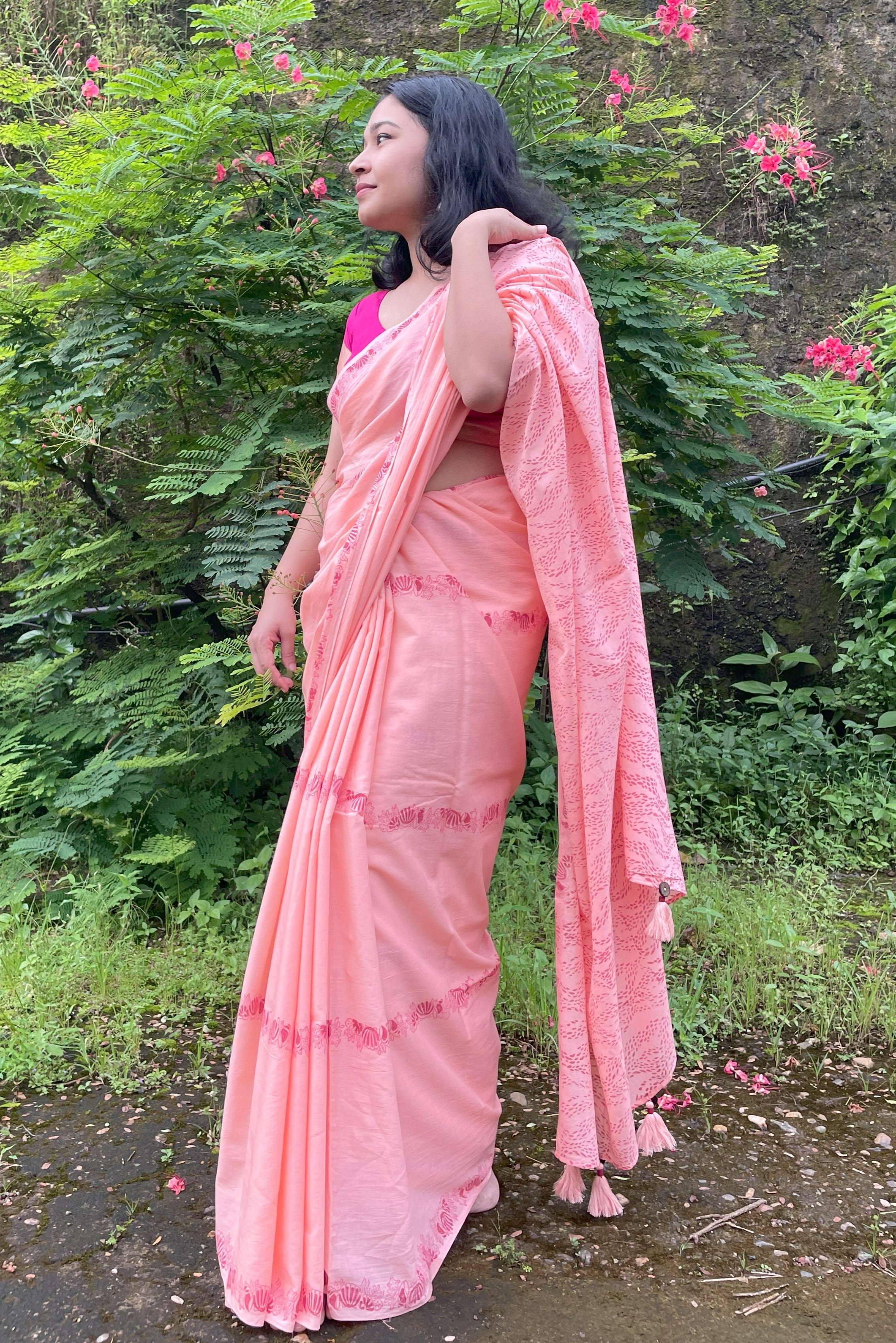Woman in a peach Mogasu saree standing outdoors with greenery in the background in Goa.