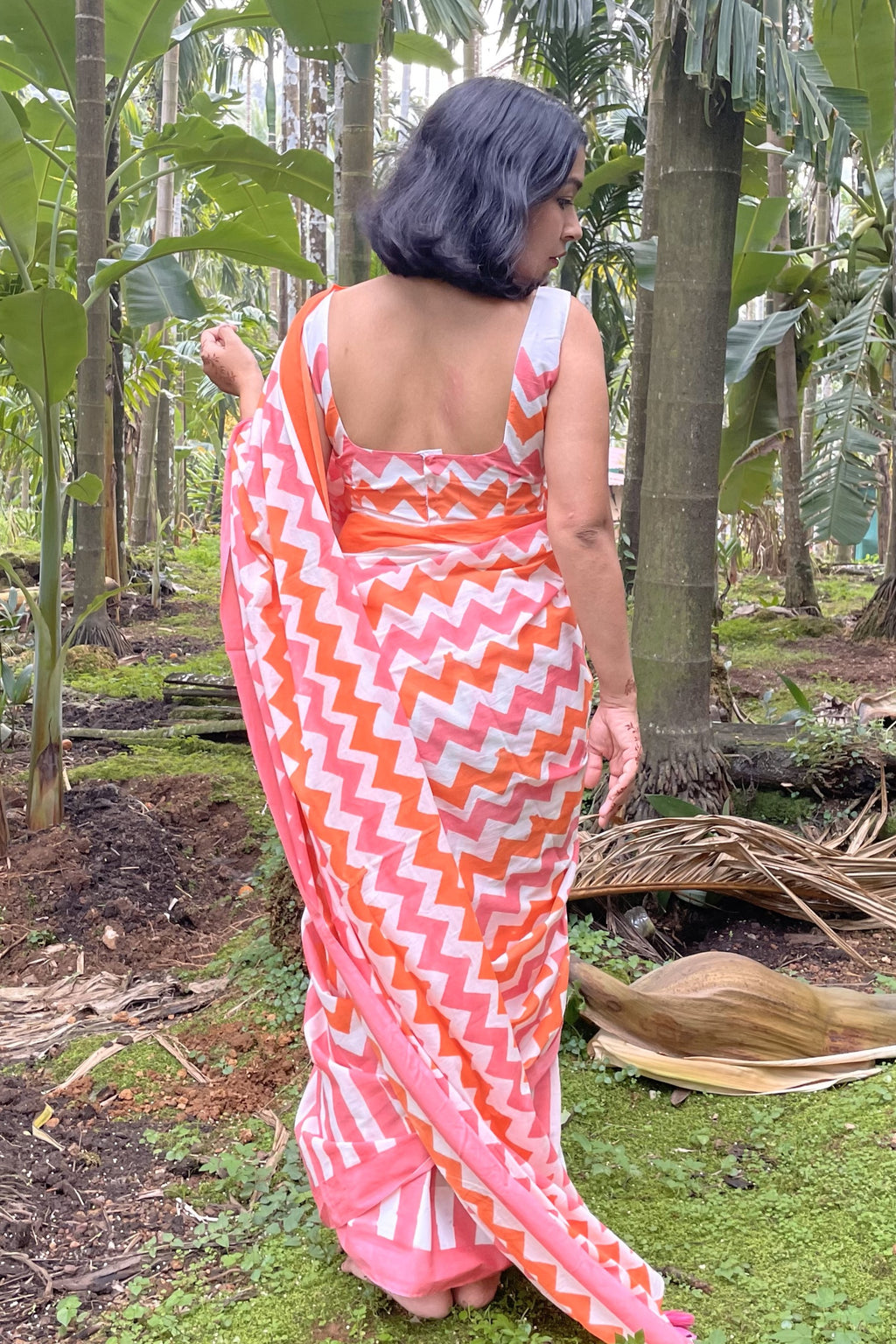 Woman in a pink and orange Mogasu chevron patterned saree standing in a forest setting.