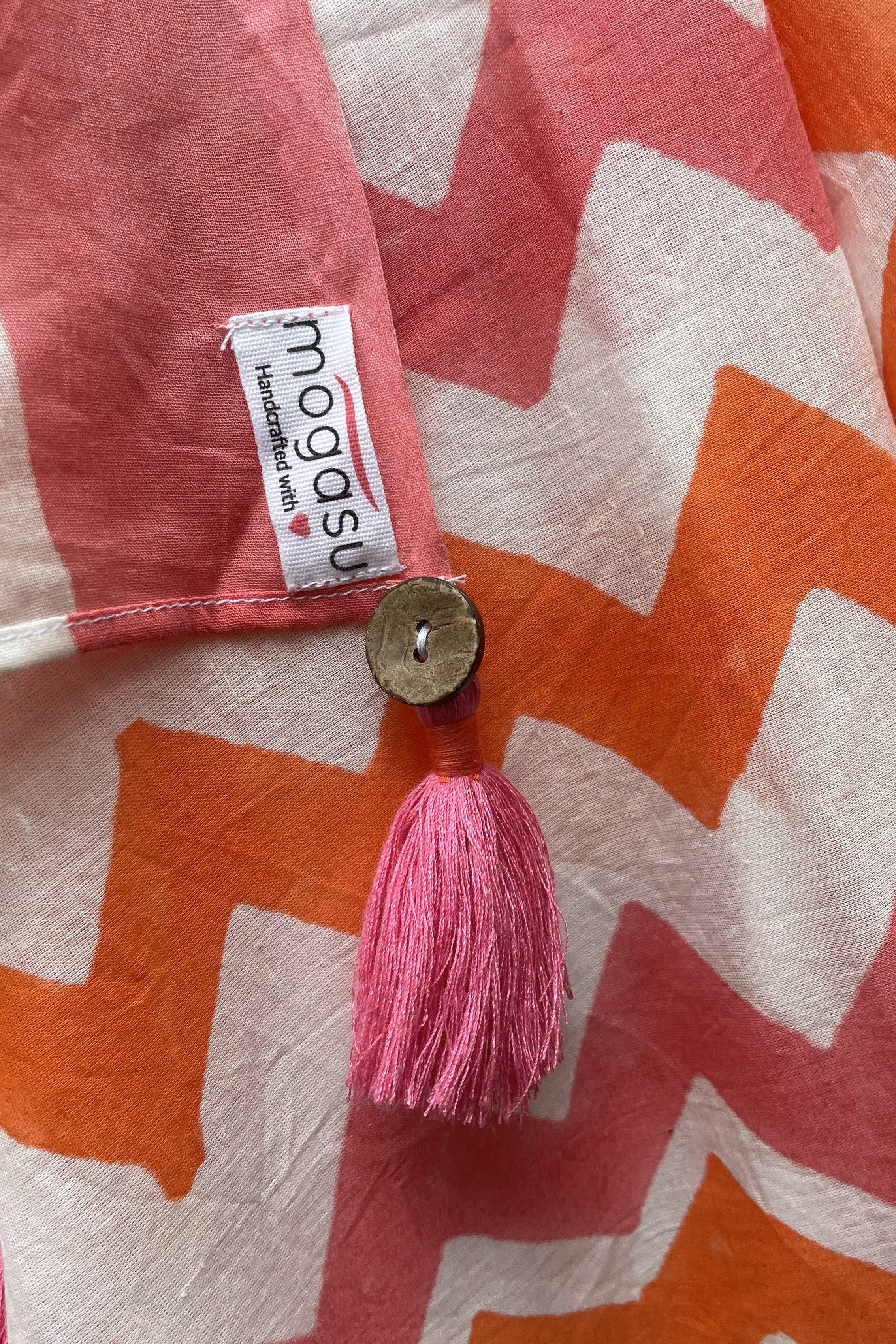 Close-up of a Mogasu saree with a pink tassel and 'mogasu' label on a patterned background.