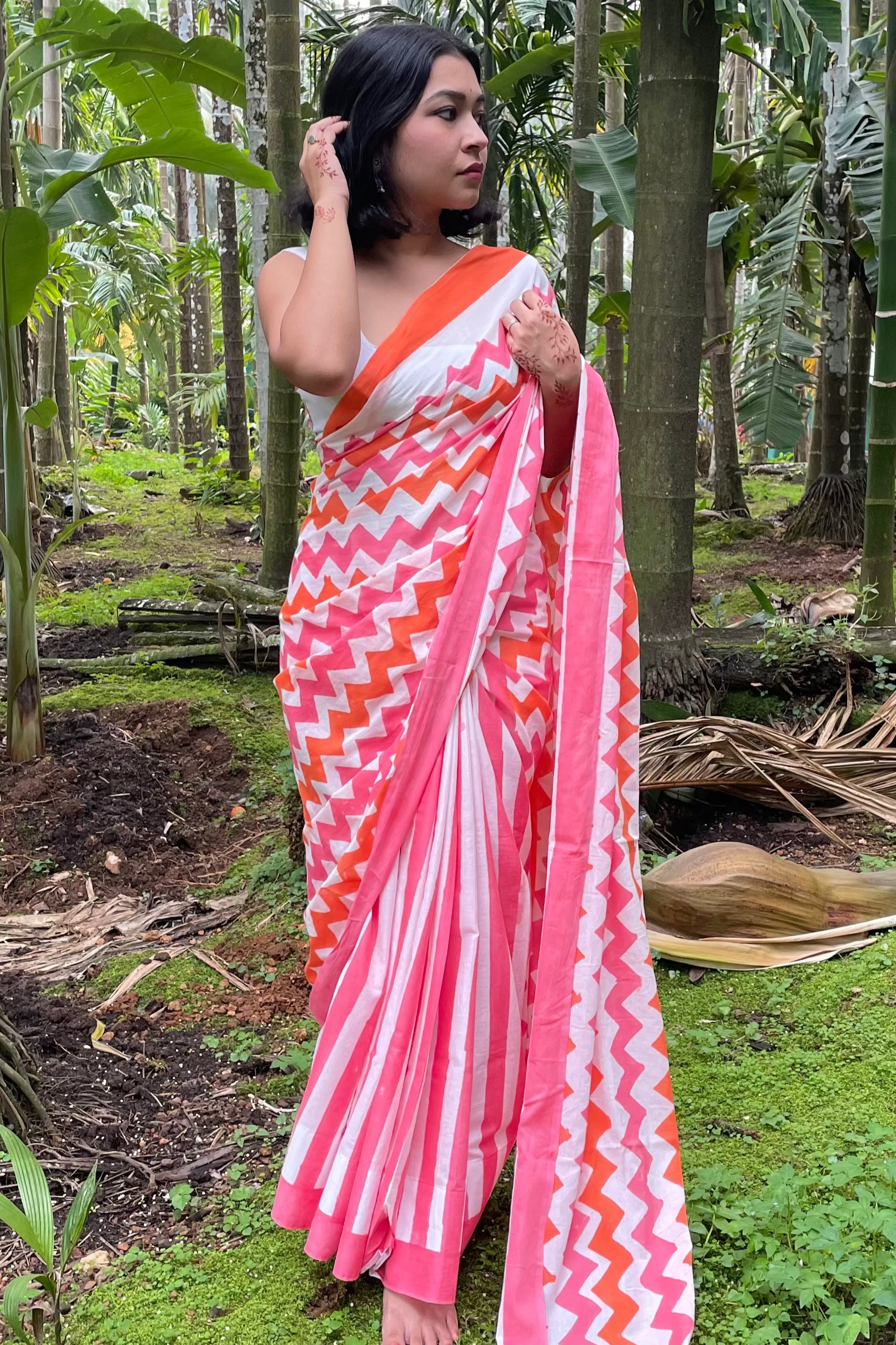 Woman wearing a pink and white Mogasu saree with orange accents in a forest setting