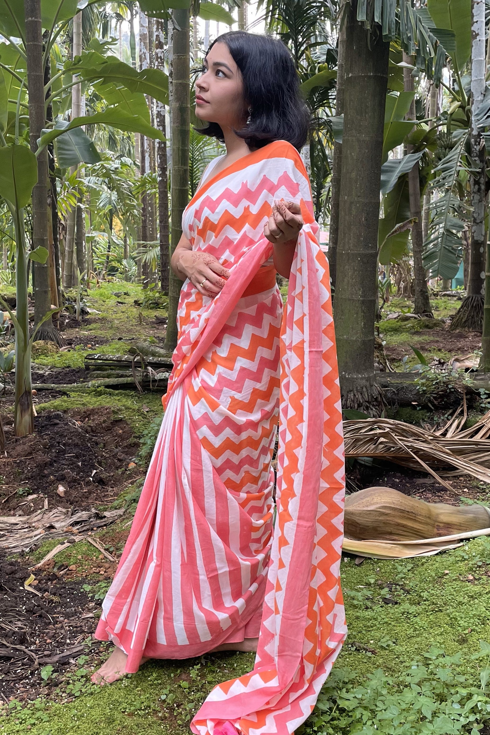 Woman in a pink and orange Mogasu Sheem mul cotton saree standing in a forest