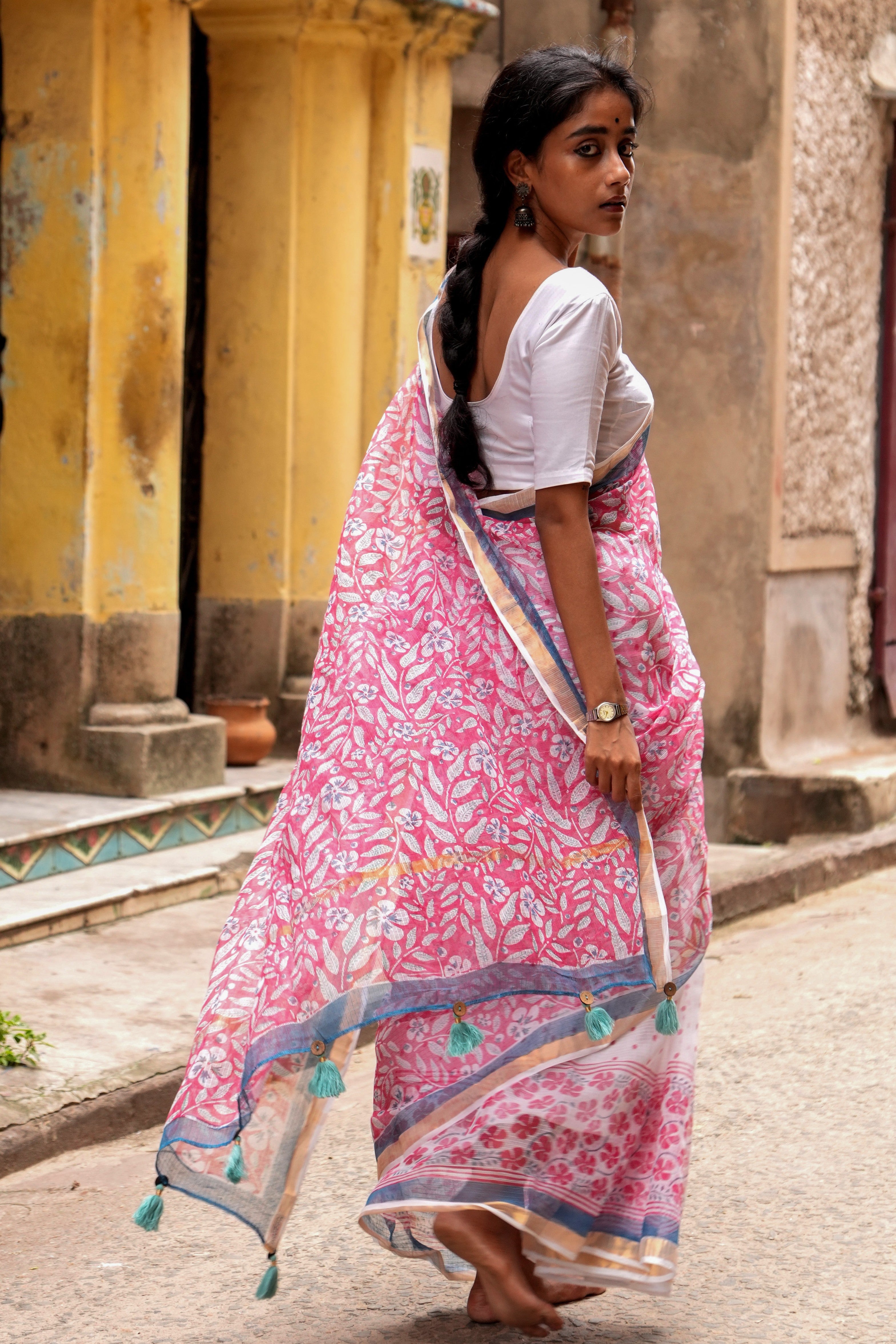 Woman in a pink Mogasu saree with a white blouse walking outdoors.